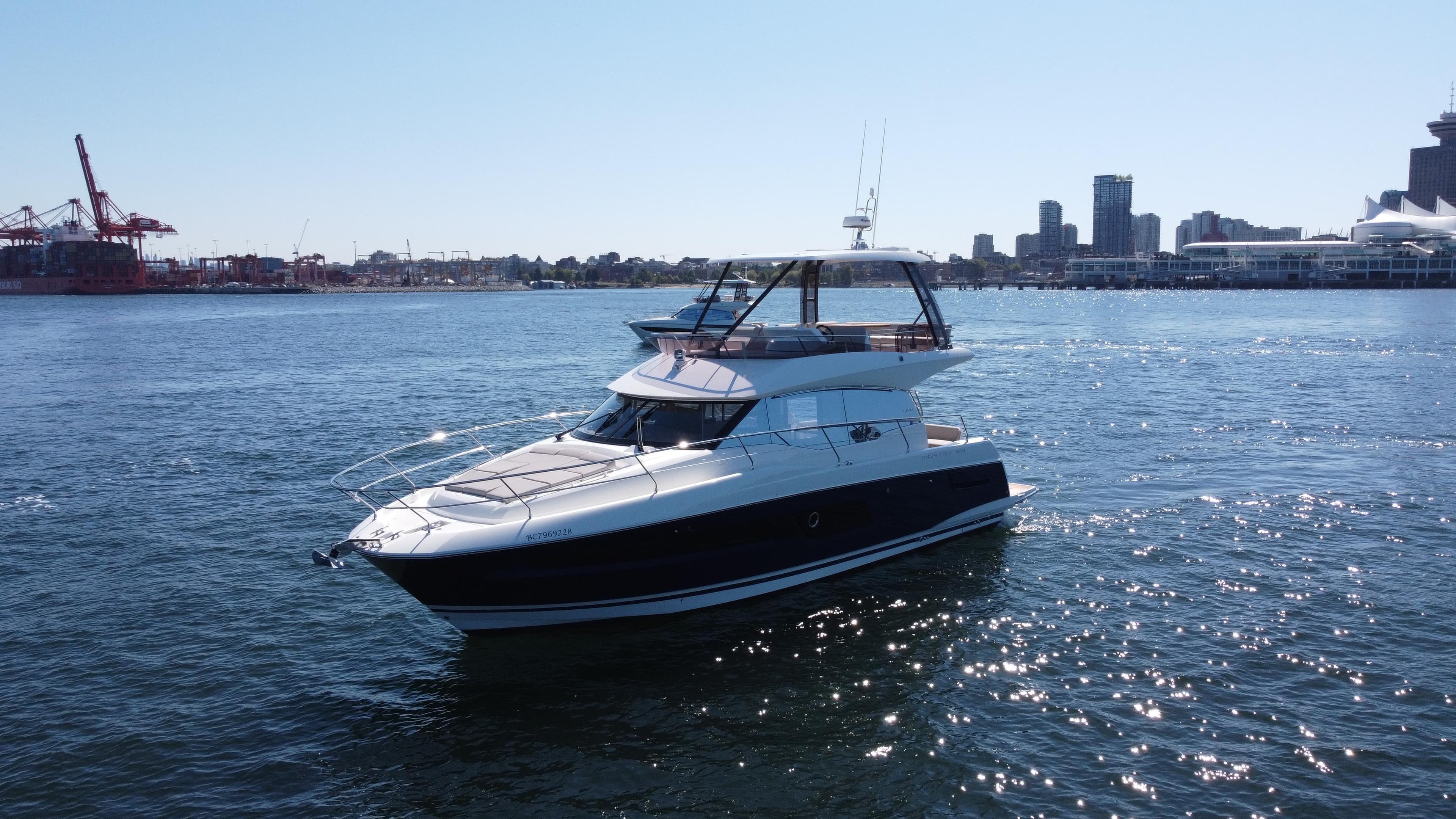 2022 Prestige 460 yacht cruising in a sunny harbor with city skyline backdrop.