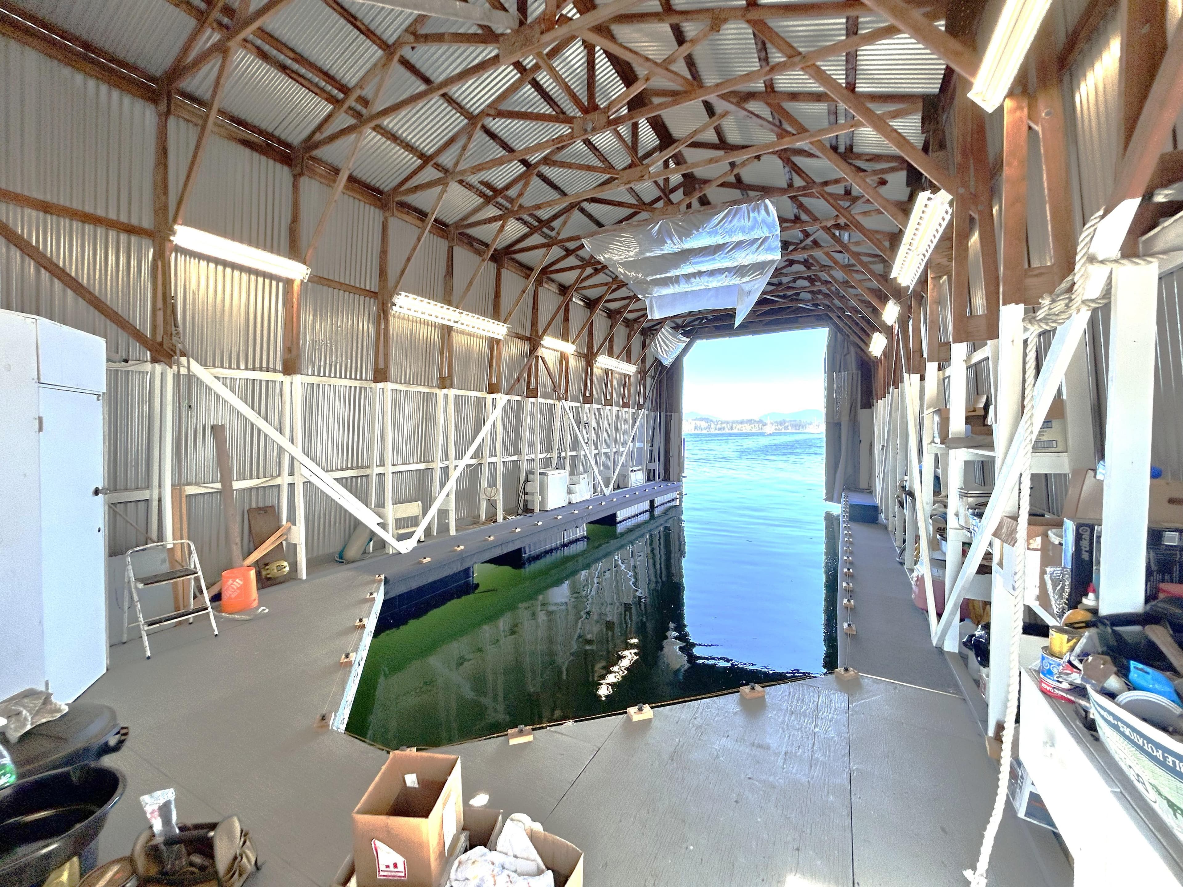 Interior view of a boathouse with water access, featuring wooden beams and storage shelves.