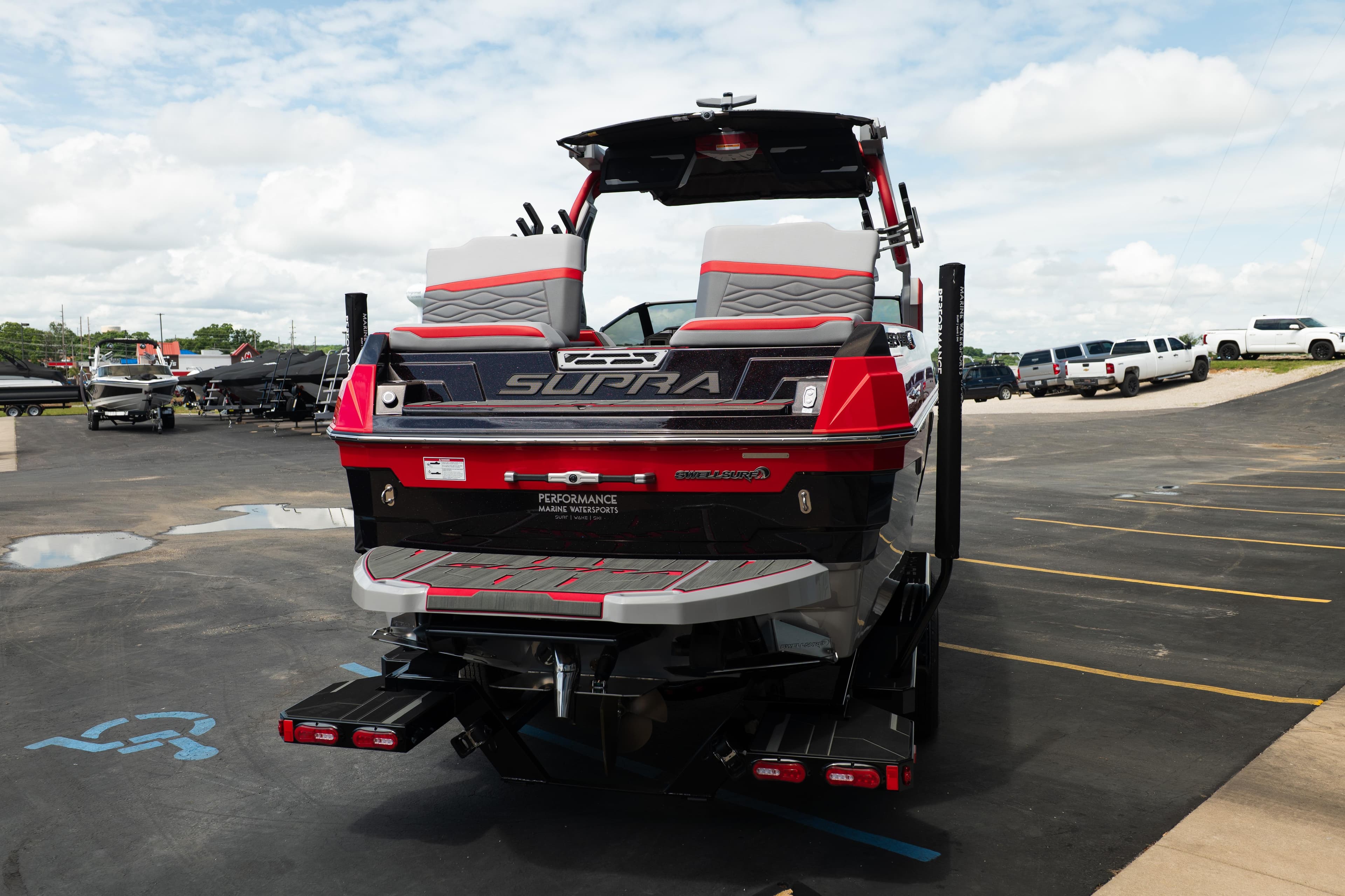2025 Supra SE boat in parking lot, rear view with vibrant red and gray design.