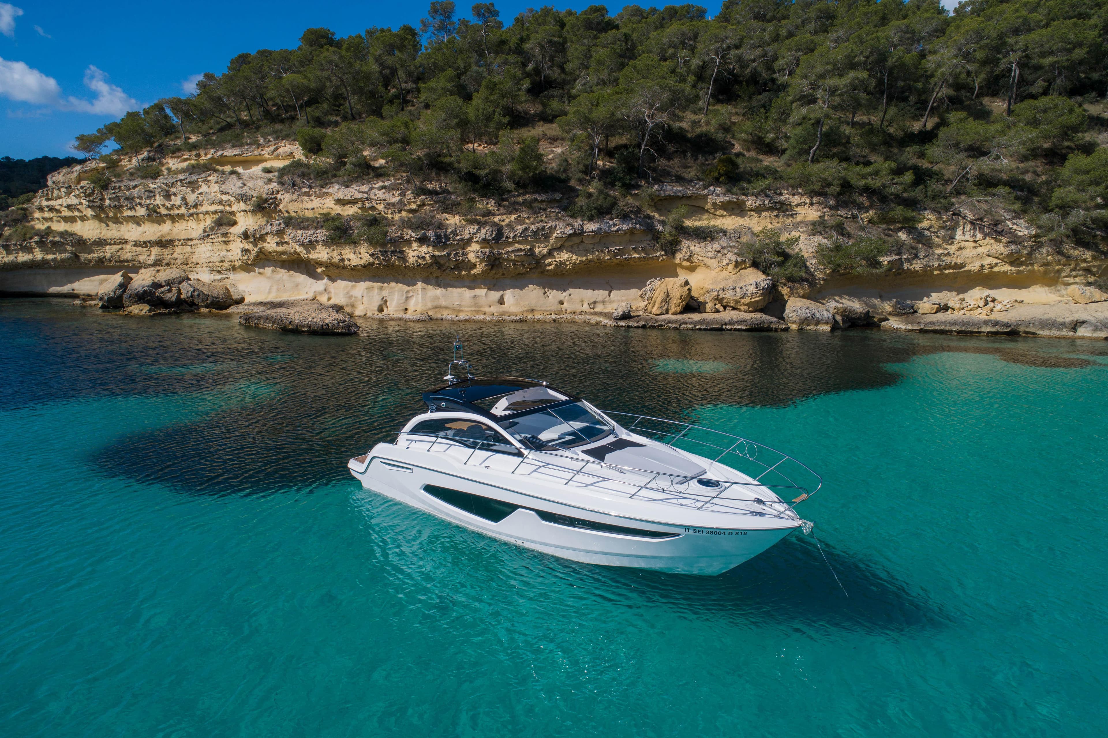 2025 Sessa Marine C38 yacht in turquoise waters near rocky coastline.
