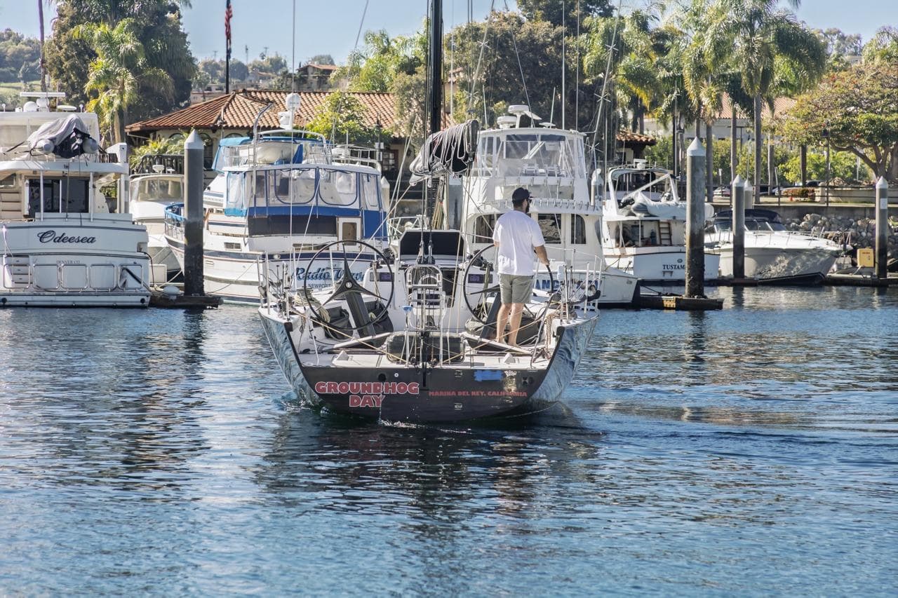 Man steering Rogers 46 sailboat in marina, surrounded by yachts and palm trees, 2007 model.