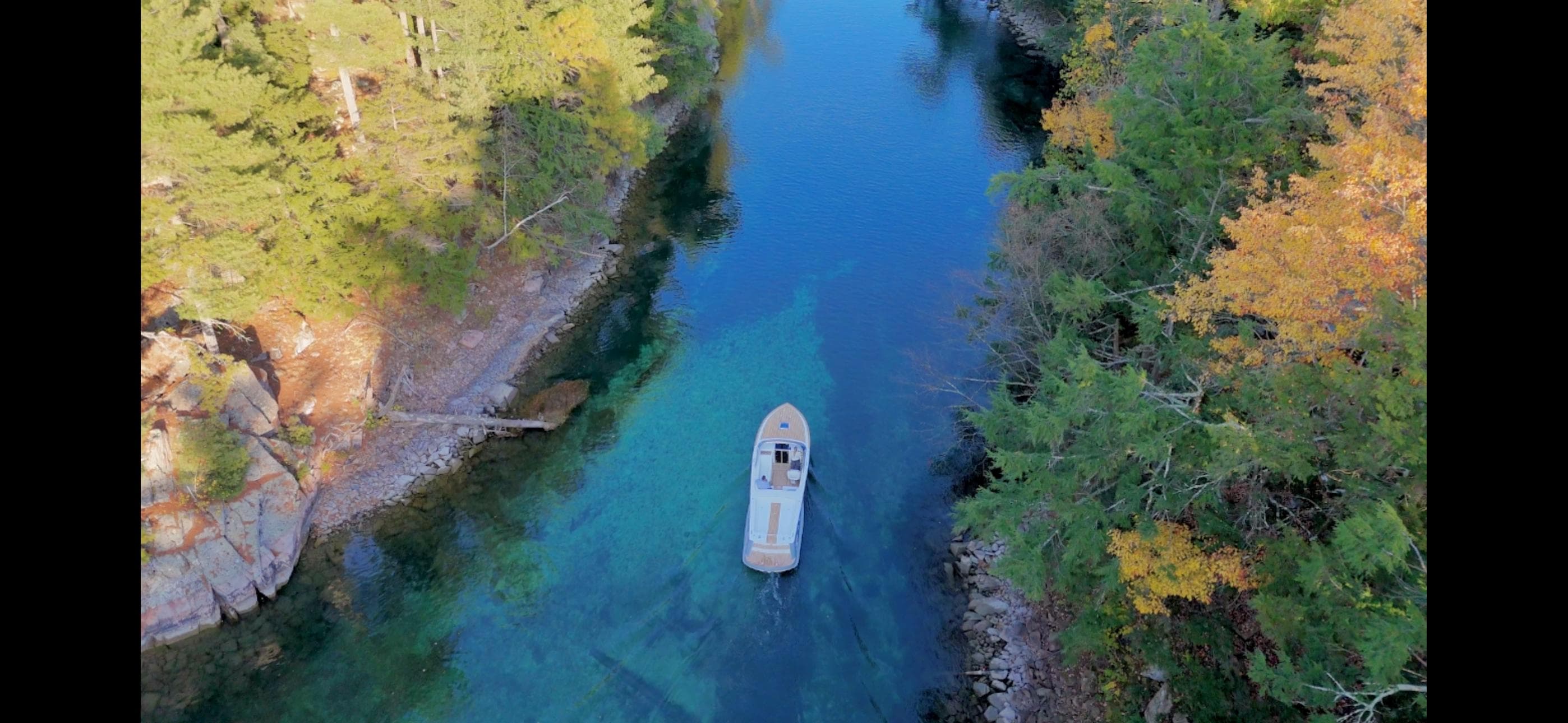 Aerial view of 2024 Comitti Venezia V28 boat on a clear, forest-lined river.