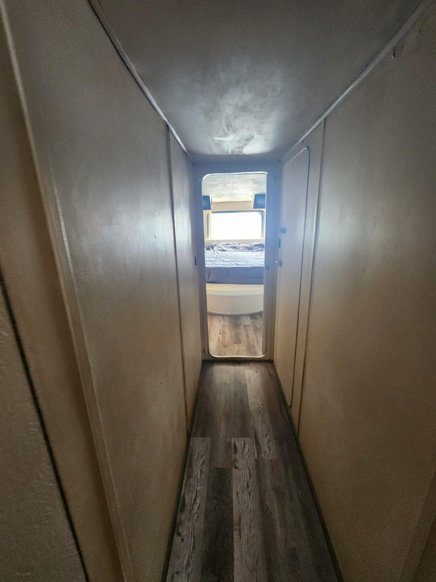 Narrow hallway in 1984 Infinity Express RV leading to a bedroom with wood flooring.