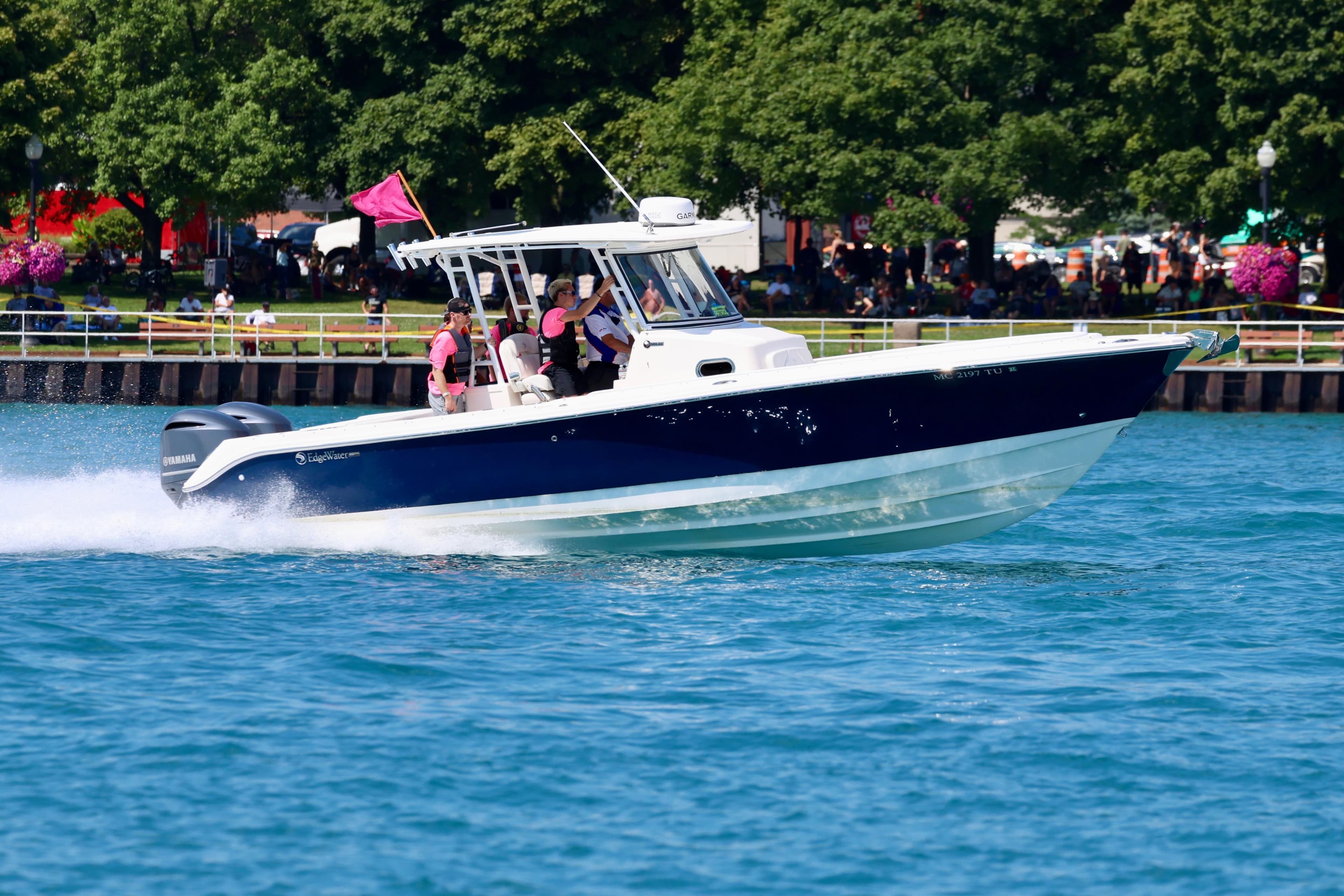 2015 Edgewater 320CC boat cruising on a sunny day near a park shoreline.