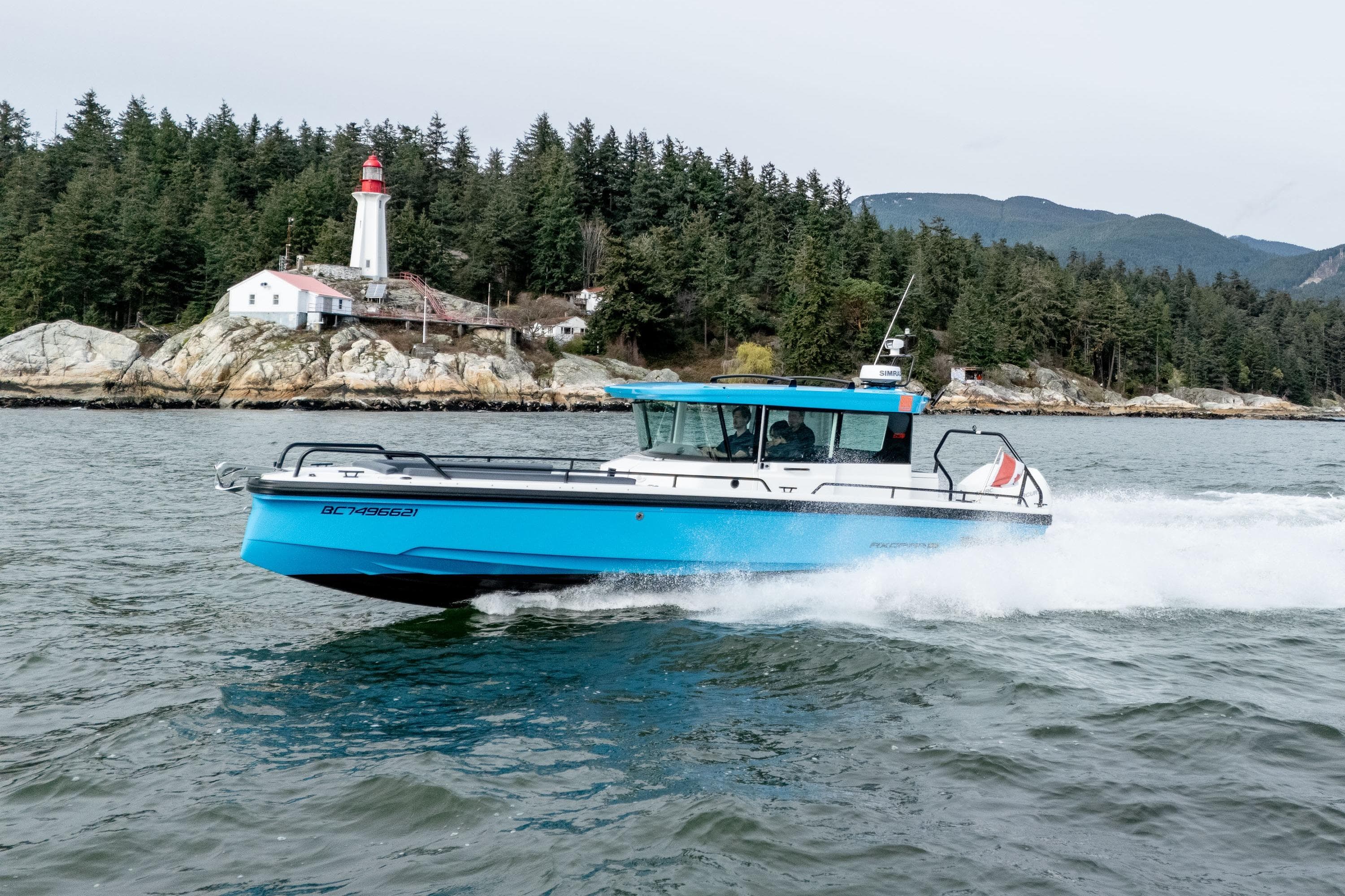 2021 Axopar 28 Cabin boat cruising near a lighthouse and forested shoreline.