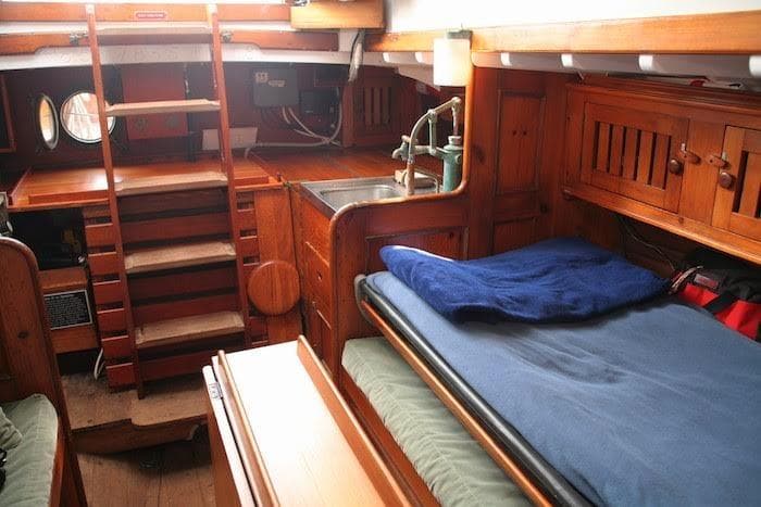 1958 Concordia Yawl interior with wooden furnishings, bed, and compact kitchen area.