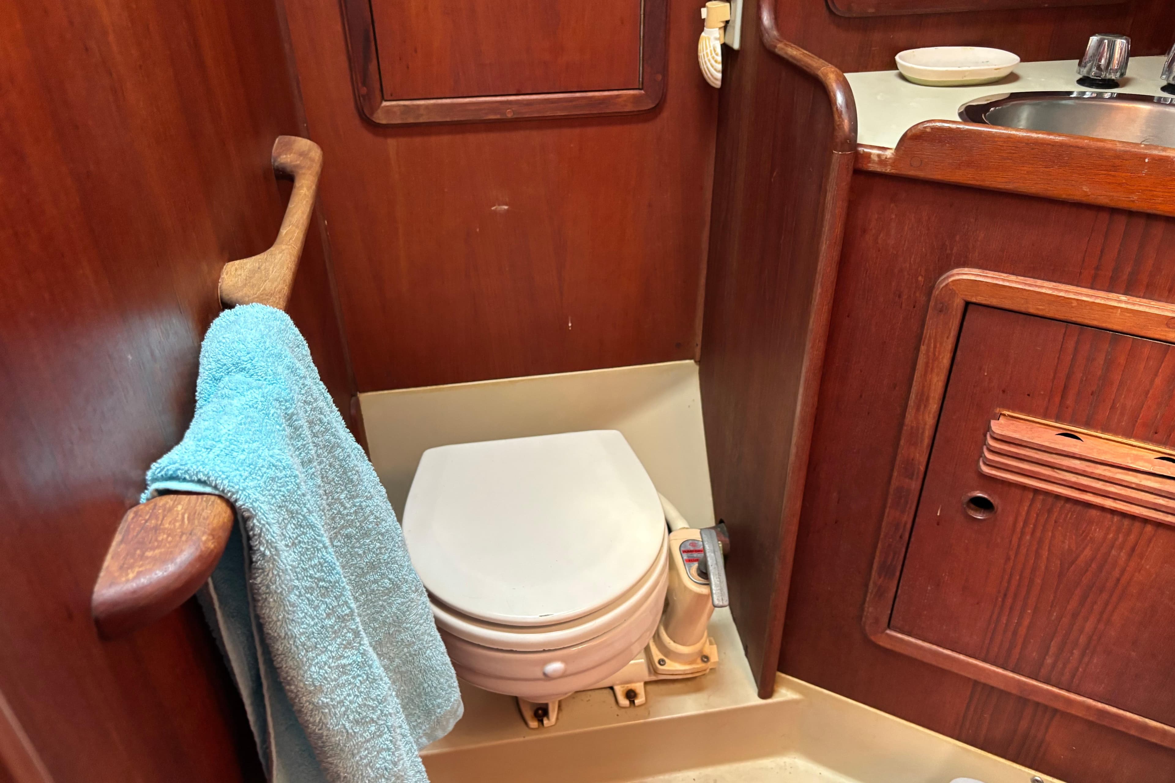 Wooden boat bathroom with toilet and sink, featuring a blue towel. C&C 40-2, 1980 model.