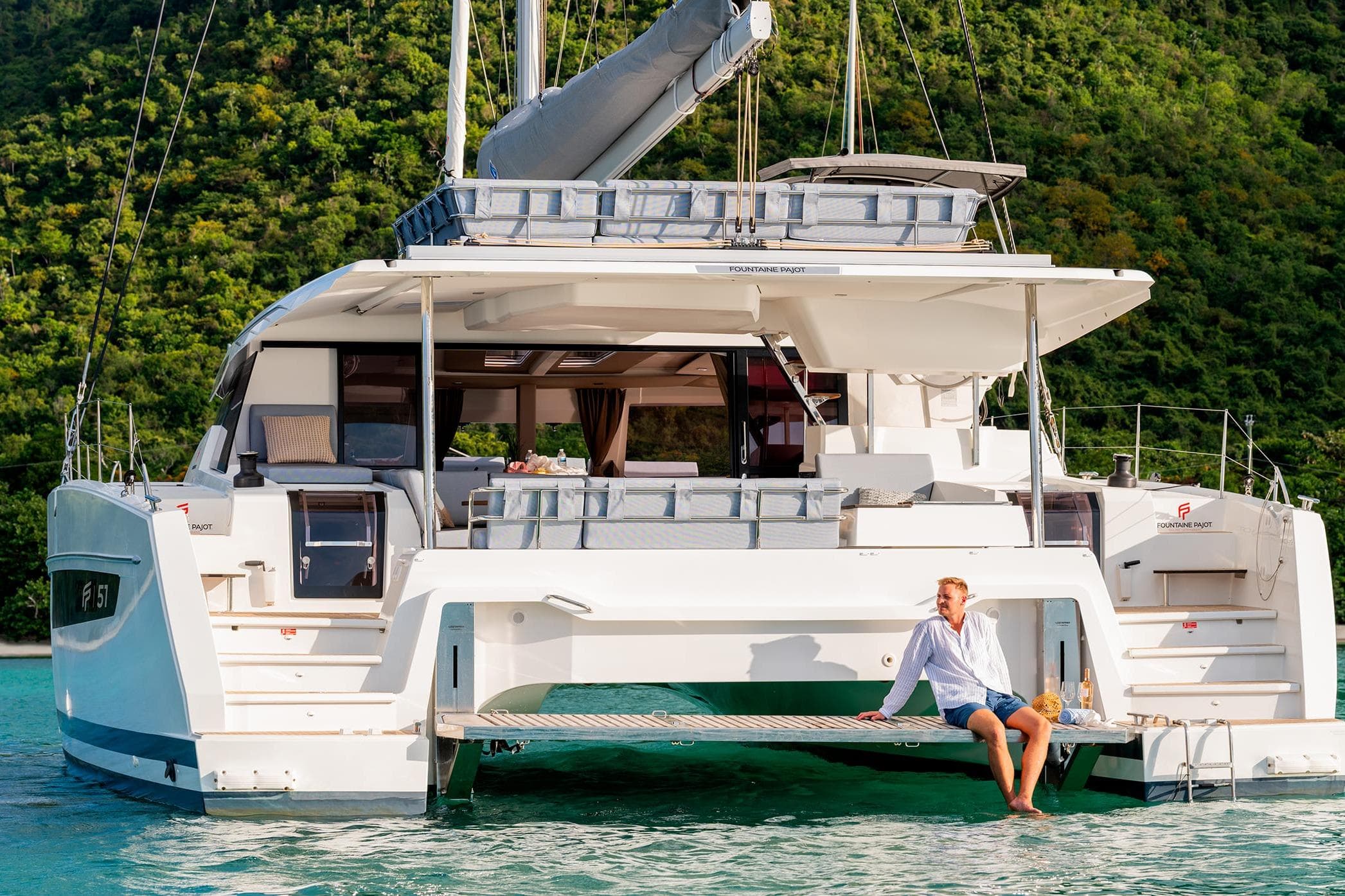 2026 Fountaine Pajot Aura 51 catamaran with a person relaxing on the deck, scenic backdrop.