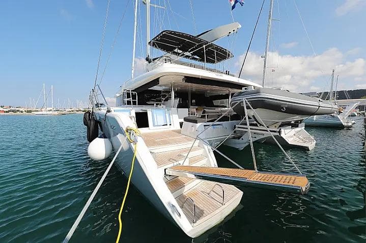 2018 Lagoon 620 Esense catamaran docked in a marina, featuring a spacious deck and tender.