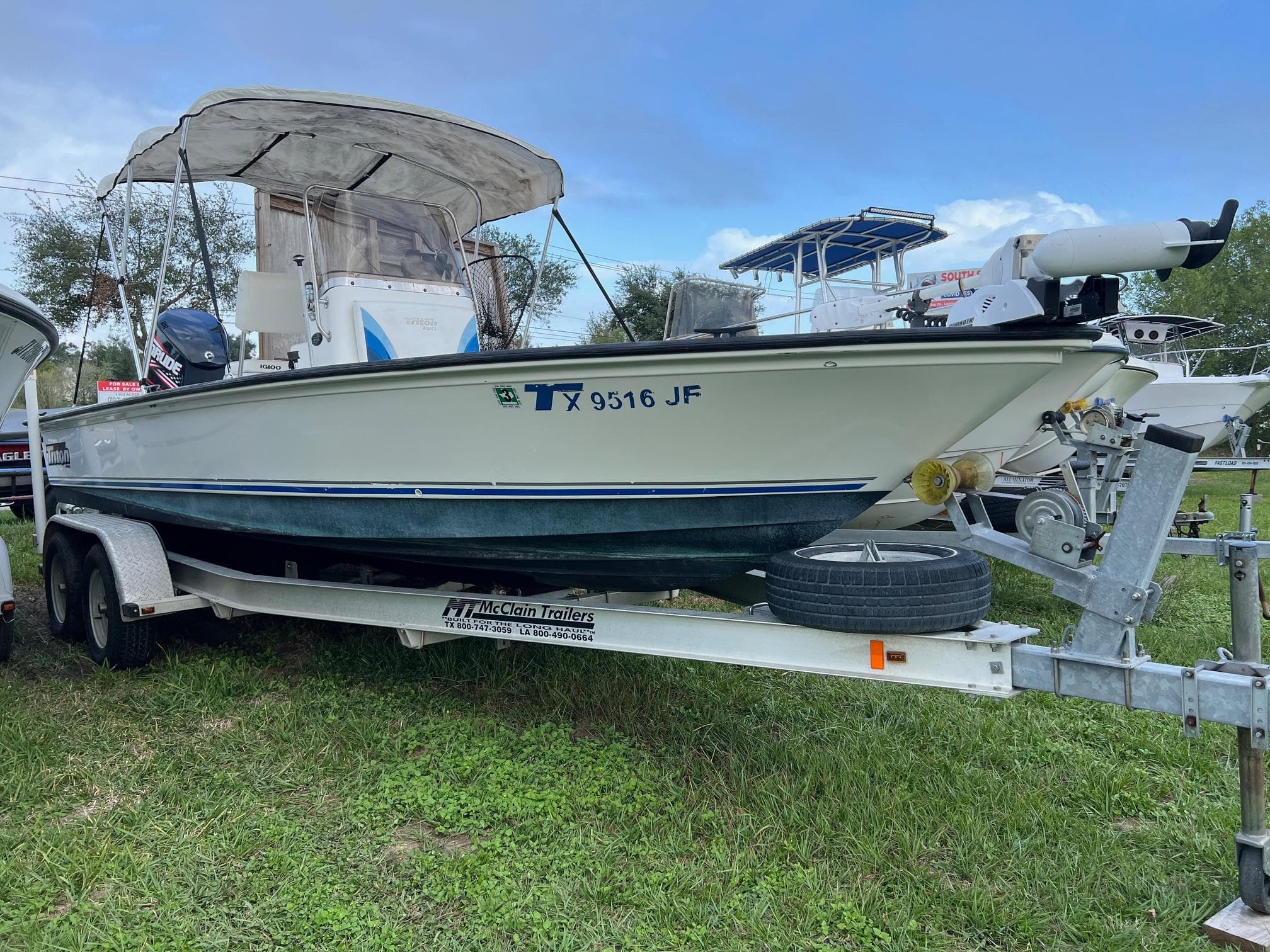 2000 Triton 23 Tunnel boat on trailer, parked on grass.