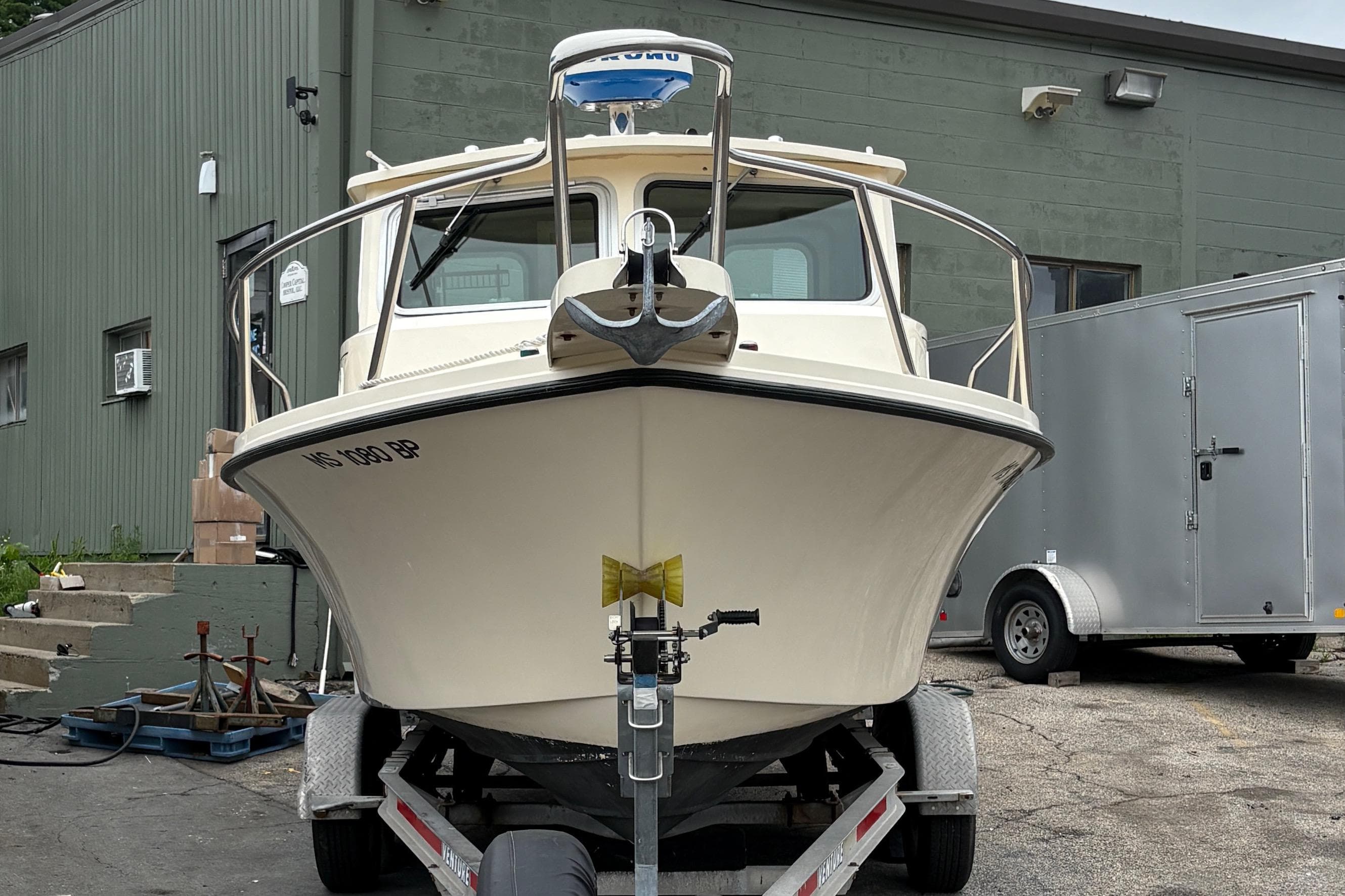2012 Parker 2120 Sport Cabin boat on trailer, parked near a green building.