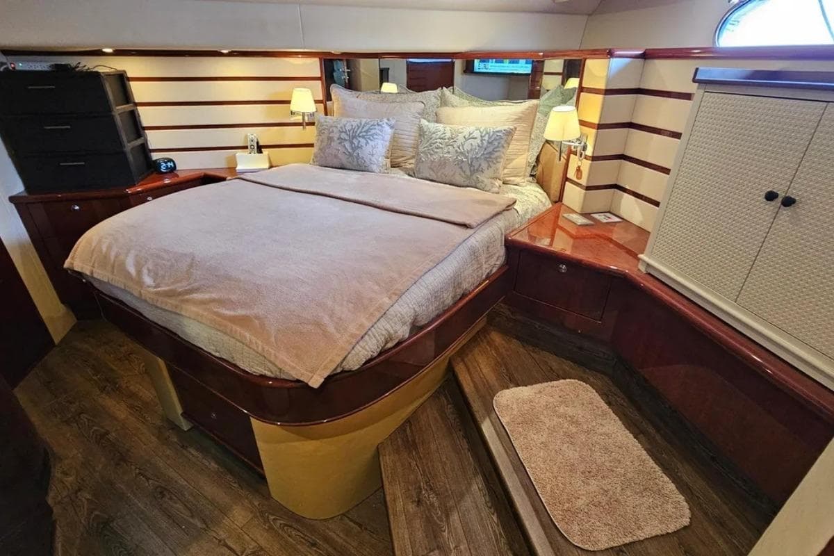 Luxurious 2005 Neptunus 56 Flybridge yacht bedroom with elegant wood finishes and cozy bedding.