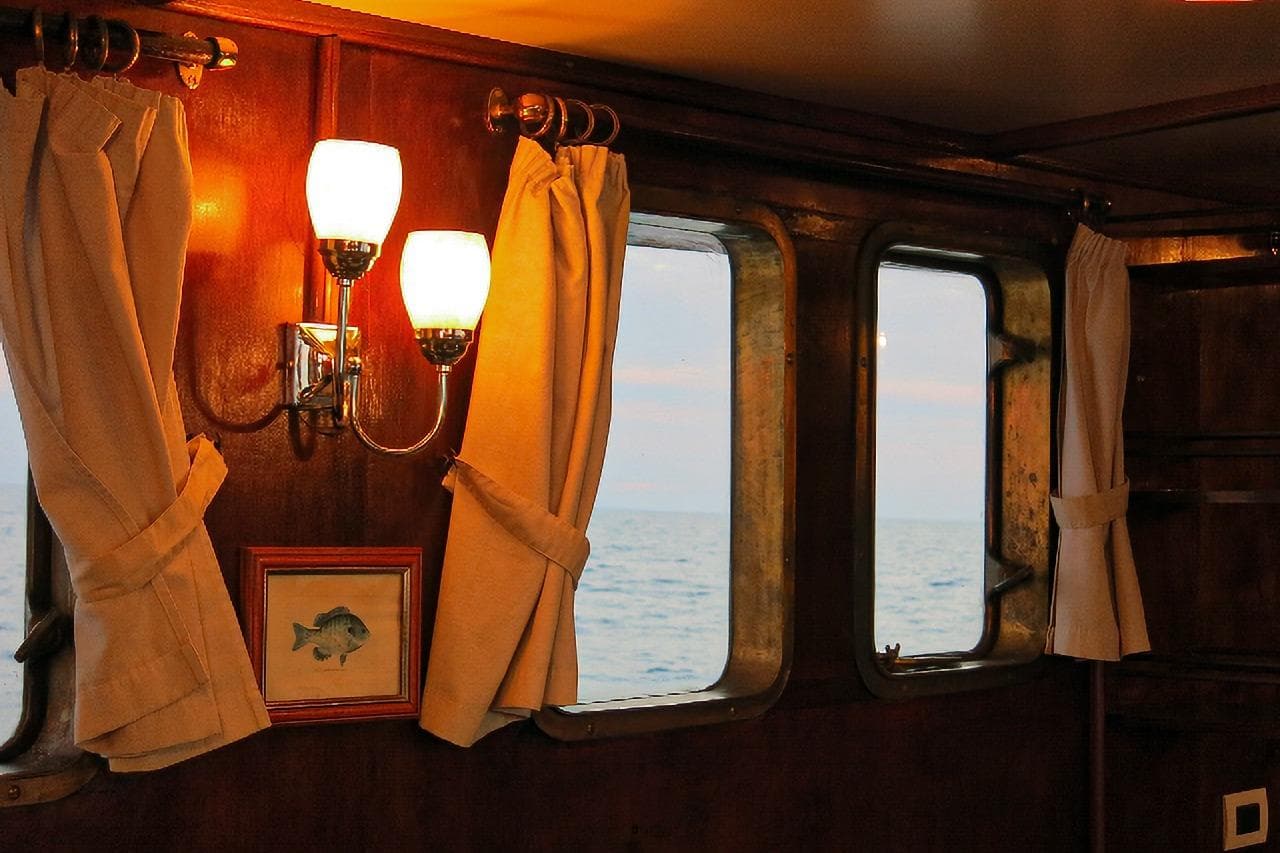 Interior of 1935 Peschereccio Diporto 20 boat with curtains, framed fish art, and sea view.