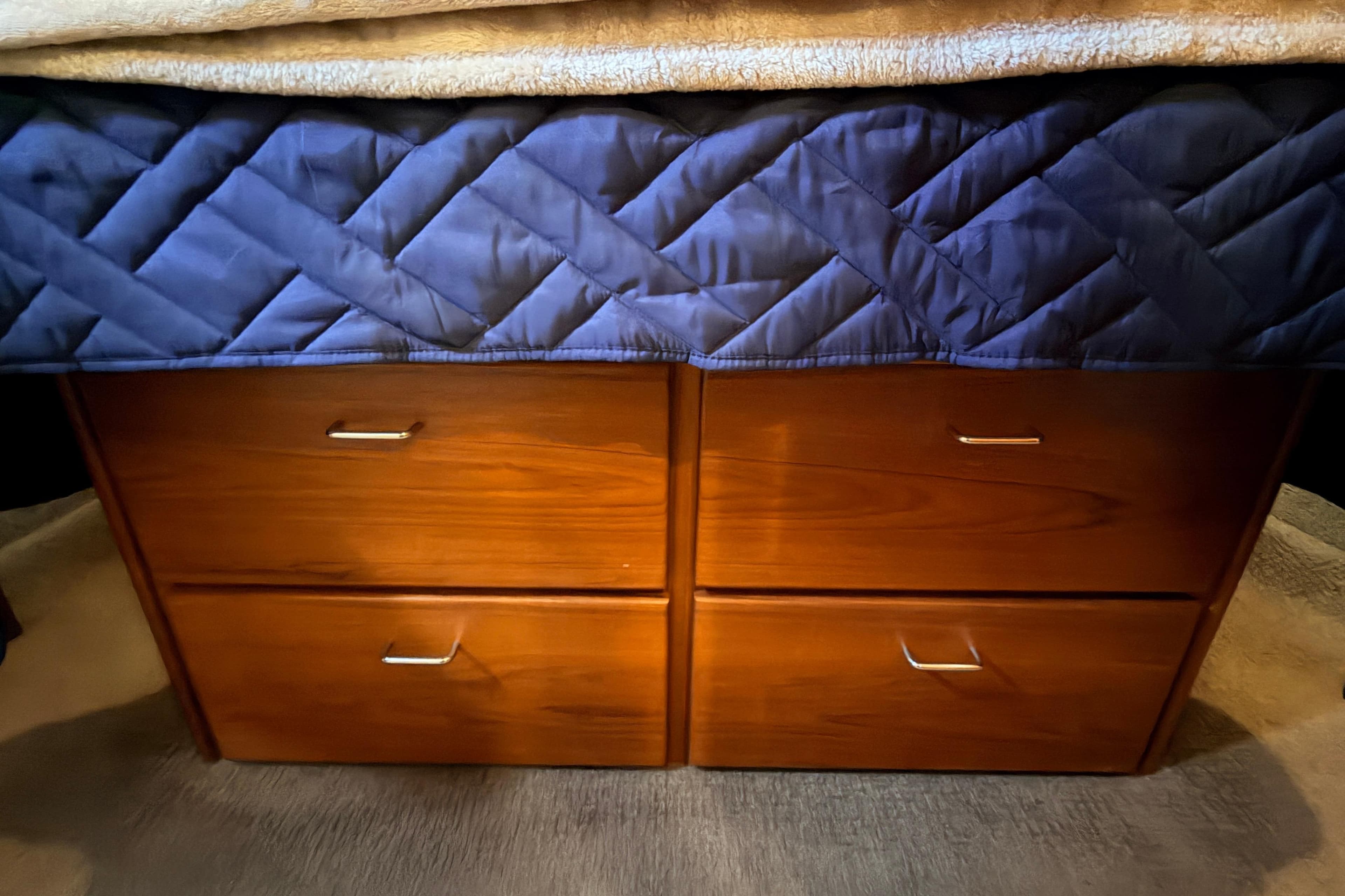 Wooden drawers under a quilted bed cover in a 2002 American Tug 34 boat.
