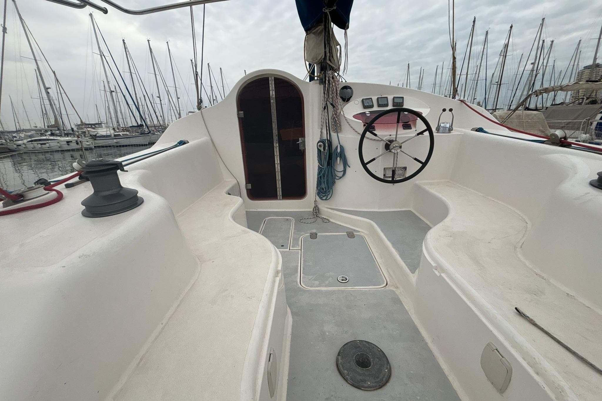 1998 Prout 38 sailboat cockpit with steering wheel, marina view, and overcast sky.