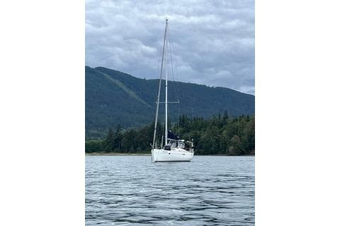 Sailboat Beneteau 473 (2006) on calm water with forested mountain backdrop.