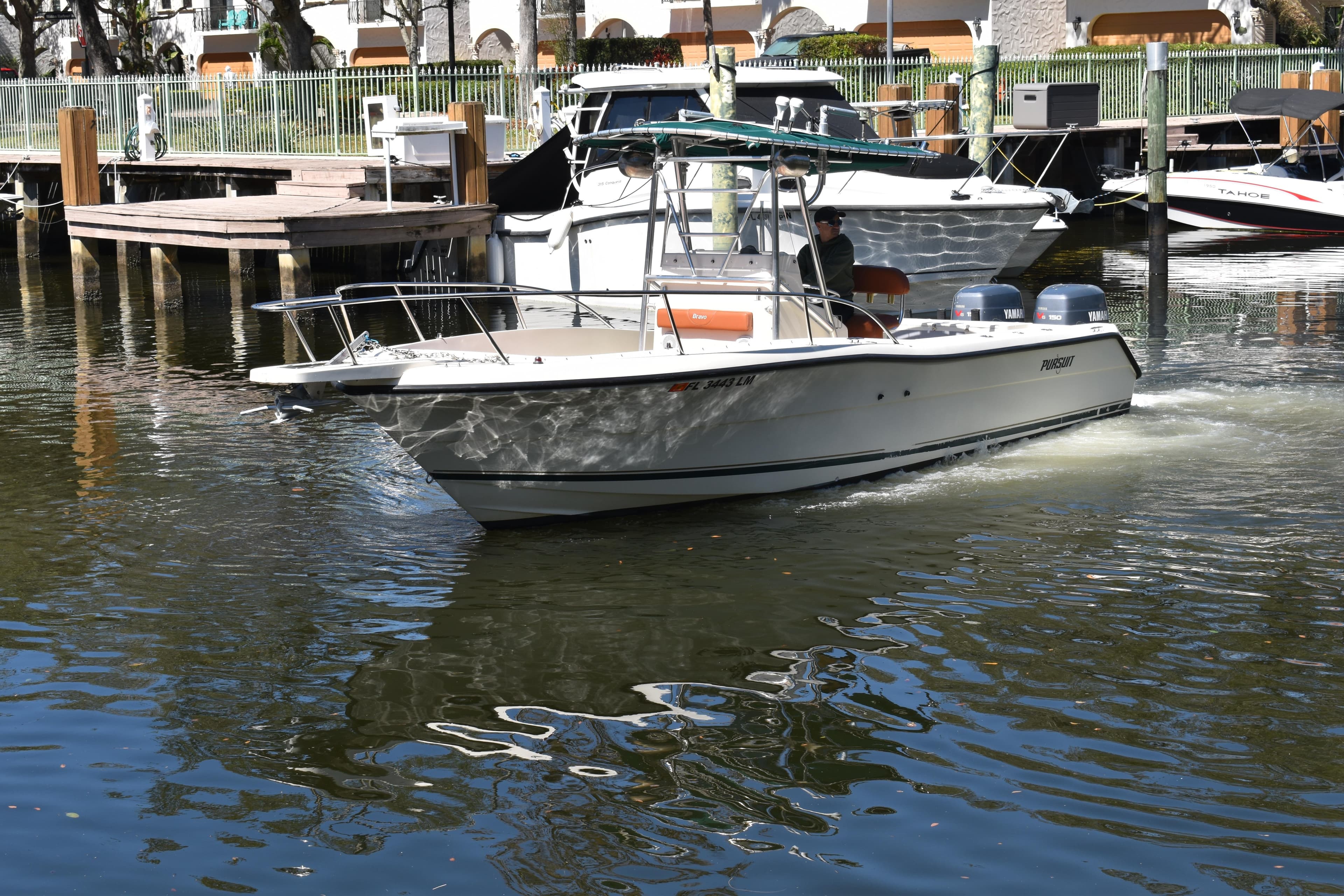 2001 Pursuit 2470 Center Console boat navigating a marina with docked vessels.