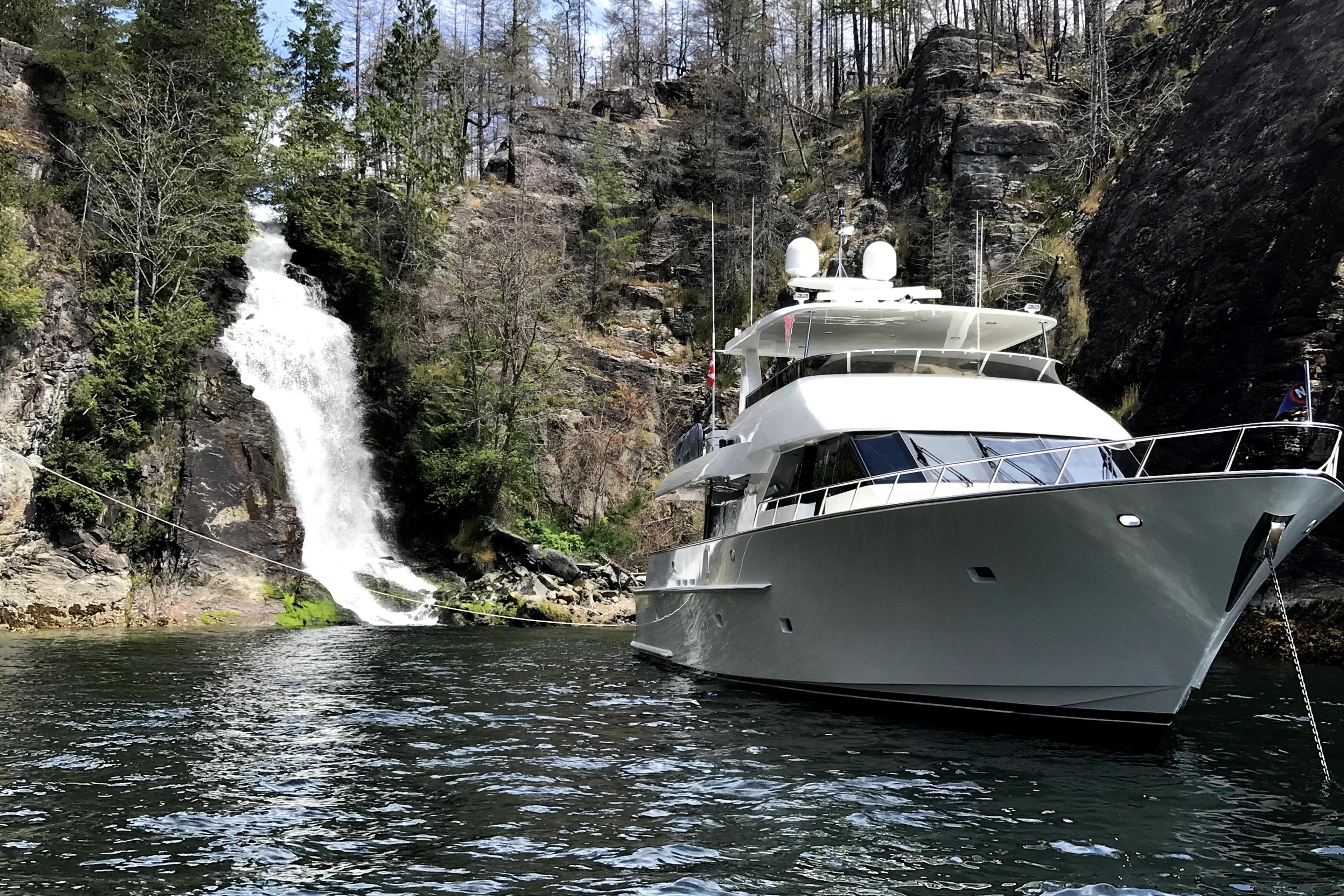 Luxury 2006 NorthCoast PILOTHOUSE yacht near scenic waterfall and rocky cliffs.