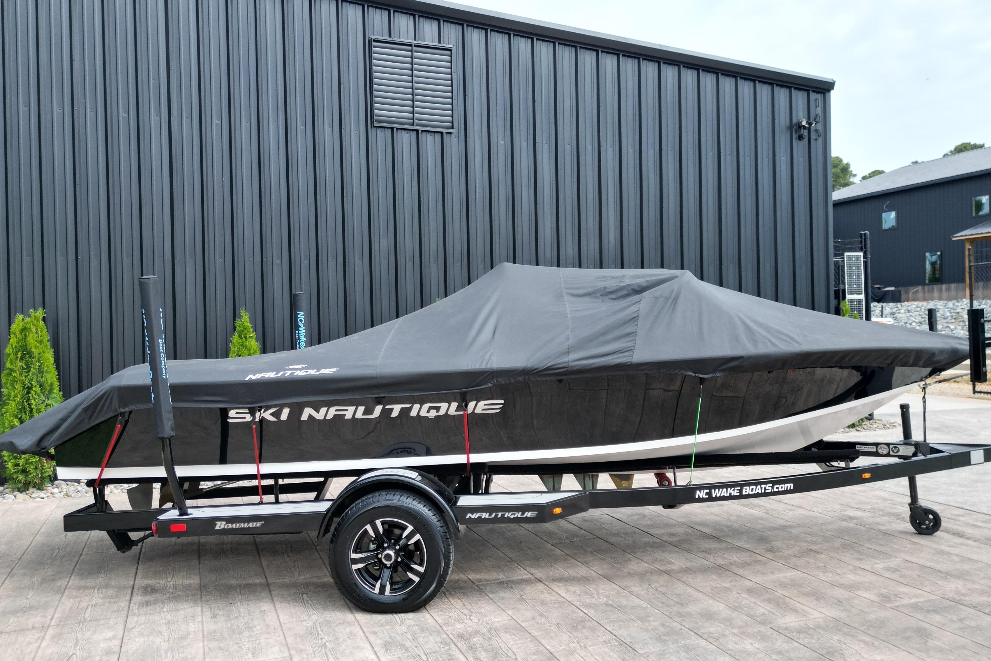 1994 Nautique Ski Nautique boat covered on trailer, parked by black building.