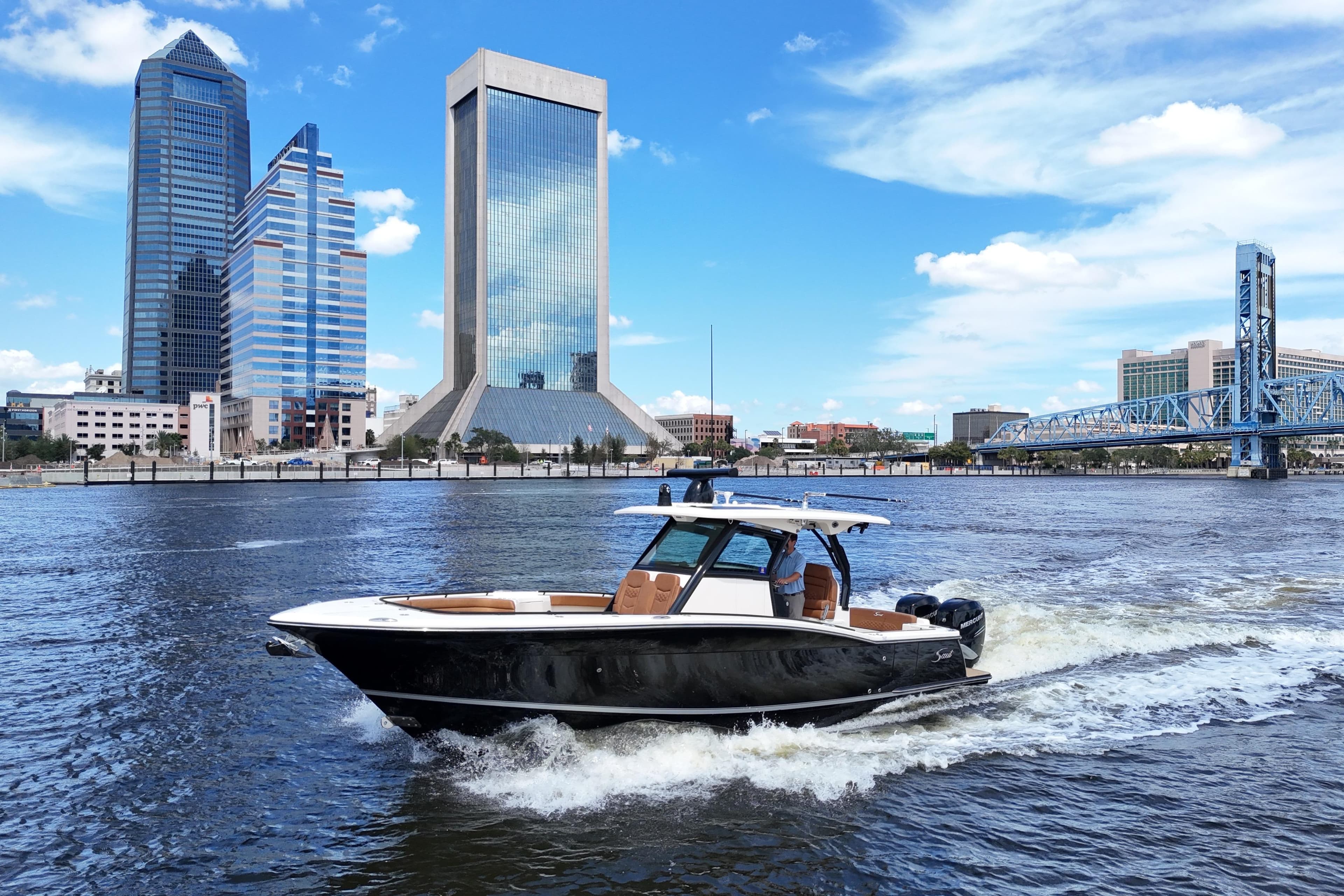 2021 Scout 330 LXF boat cruising on a river with city skyline backdrop.