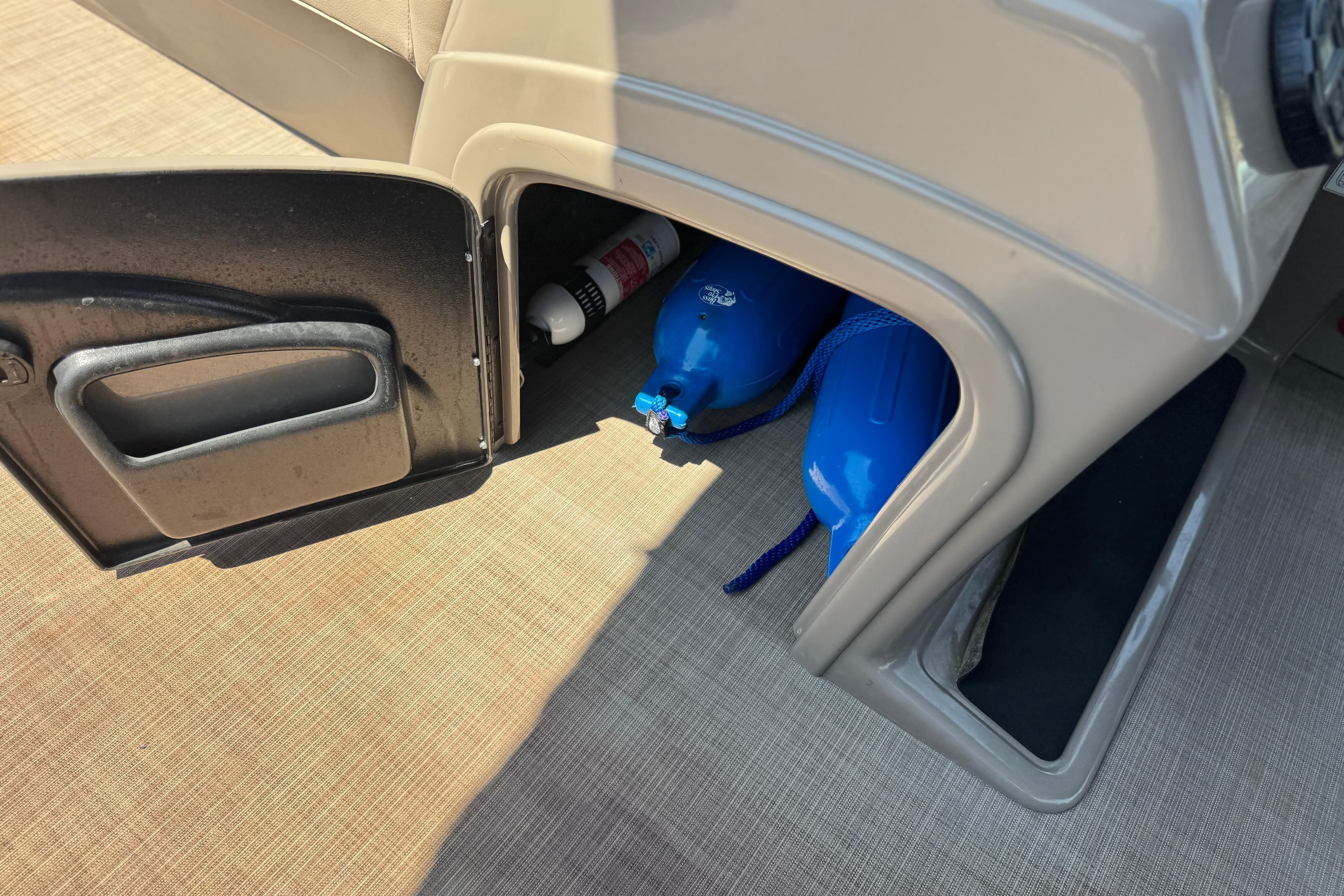 Storage compartment in a 2021 Sun Tracker SportFish 22 DLX, containing blue fenders and a fire extinguisher.