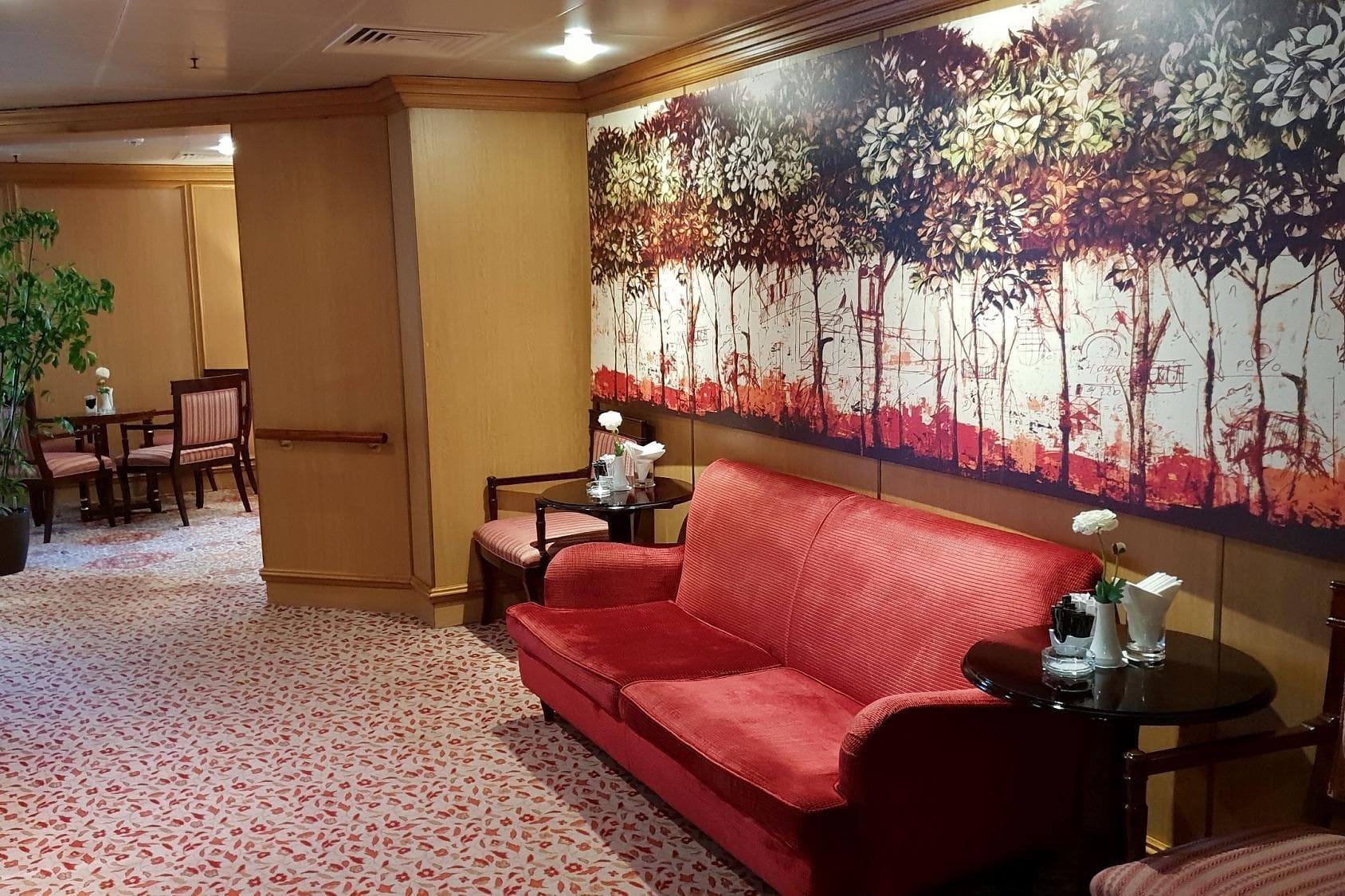 Luxurious cruise ship lounge with red sofa, artistic wall mural, and elegant decor.