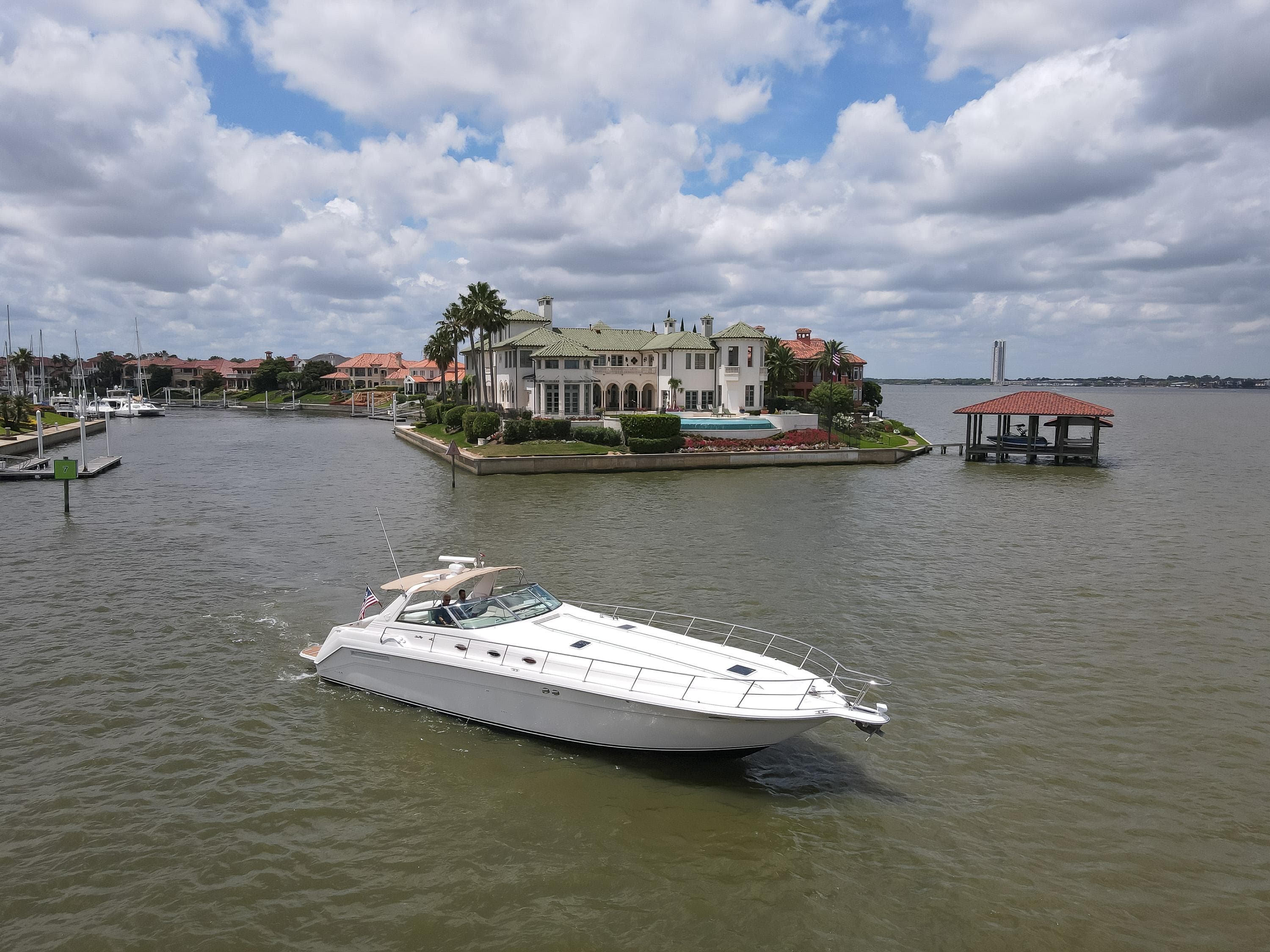 1996 Sea Ray 500 Sundancer yacht cruising near luxurious waterfront mansion.