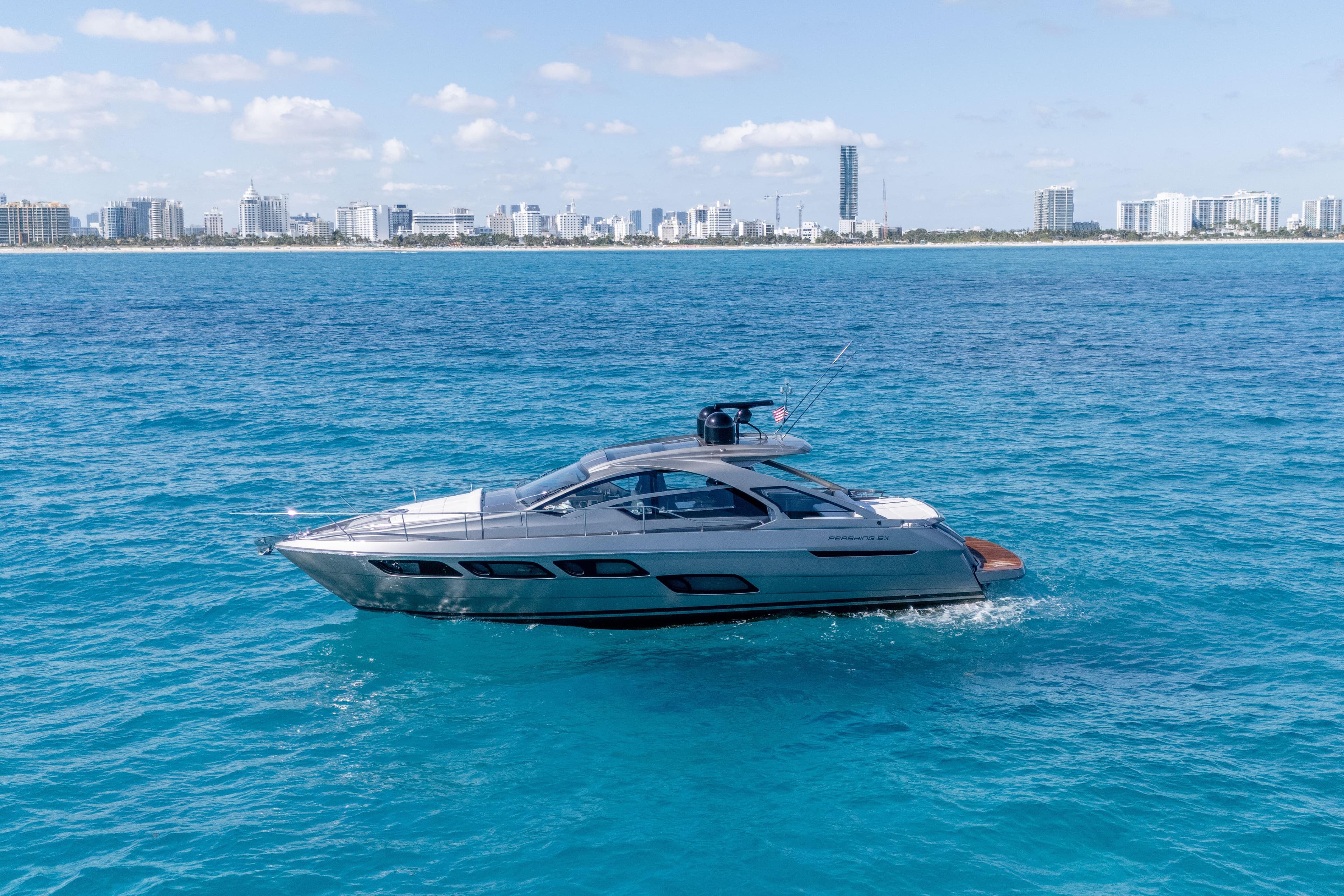 2019 Pershing 5x yacht cruising on blue ocean with city skyline in background.