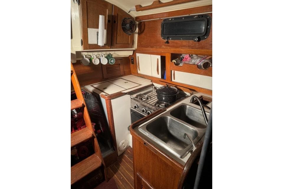 Compact kitchen in 1984 Sea Sprite 34 Yawl, featuring stove, sink, and wooden cabinetry.