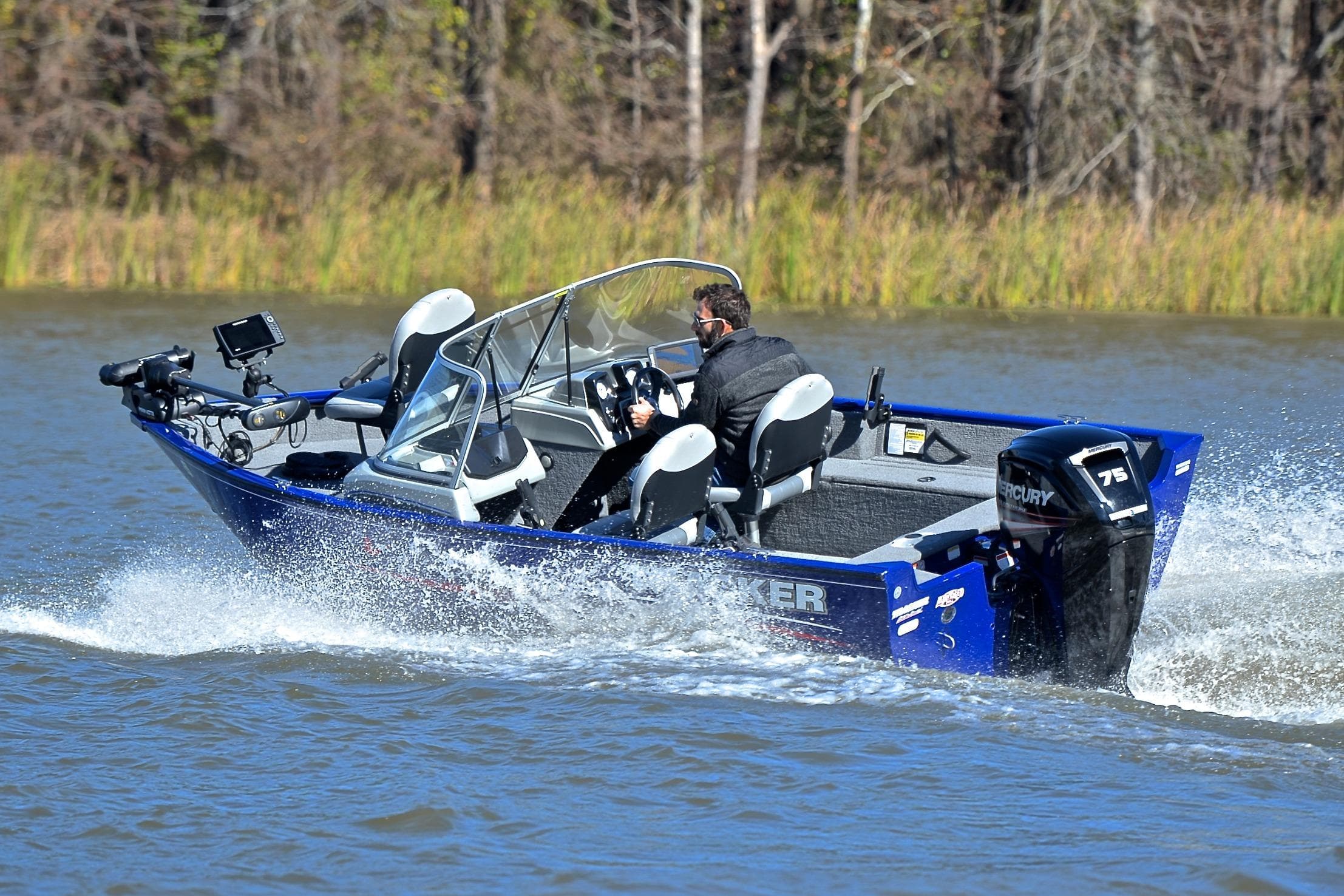 2017 Tracker Pro Guide V-16 WT boat speeding on a lake with lush greenery.