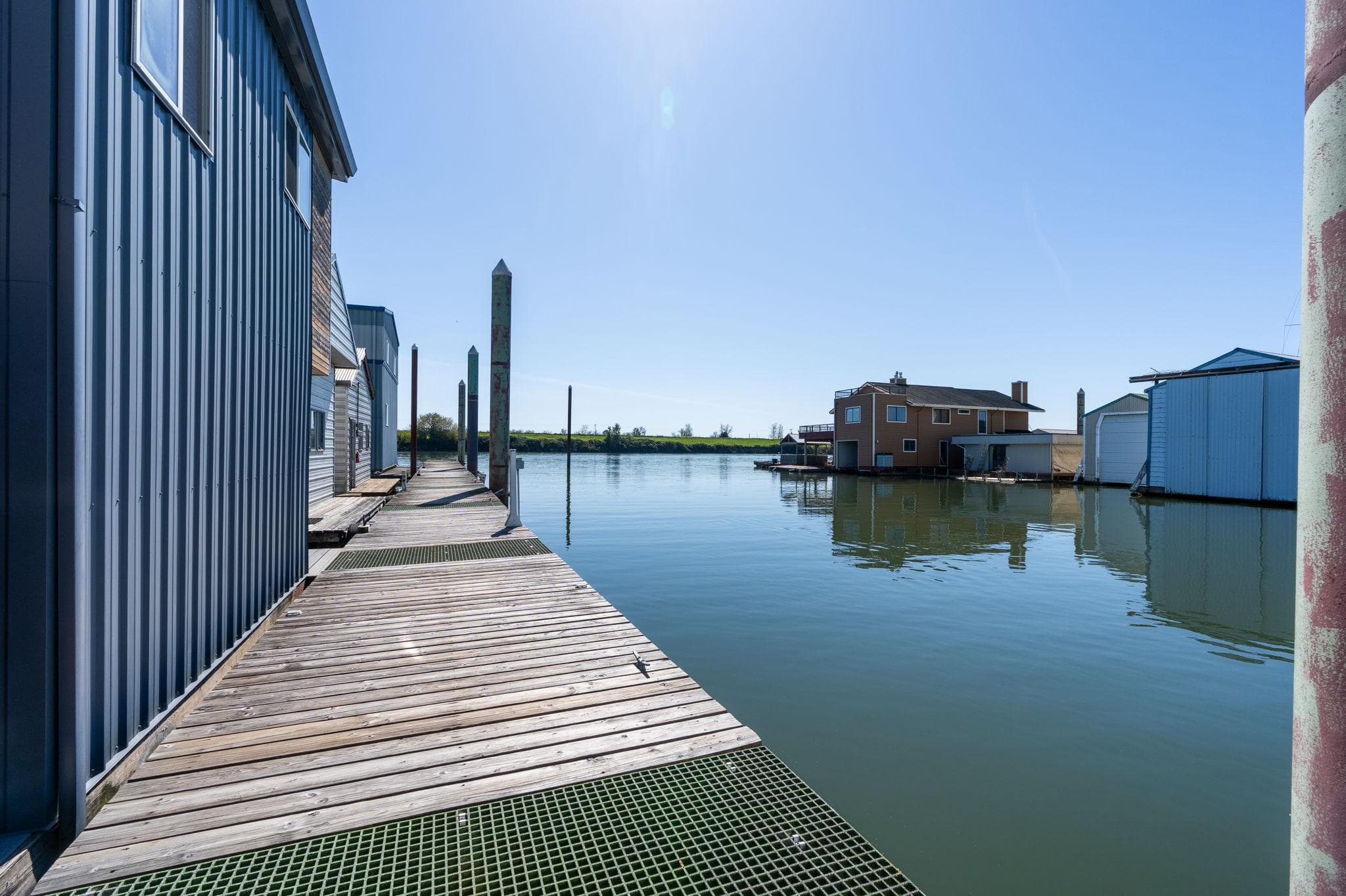 Wooden dock beside calm water at Larson Boathouse, 1985 model, under clear blue sky.