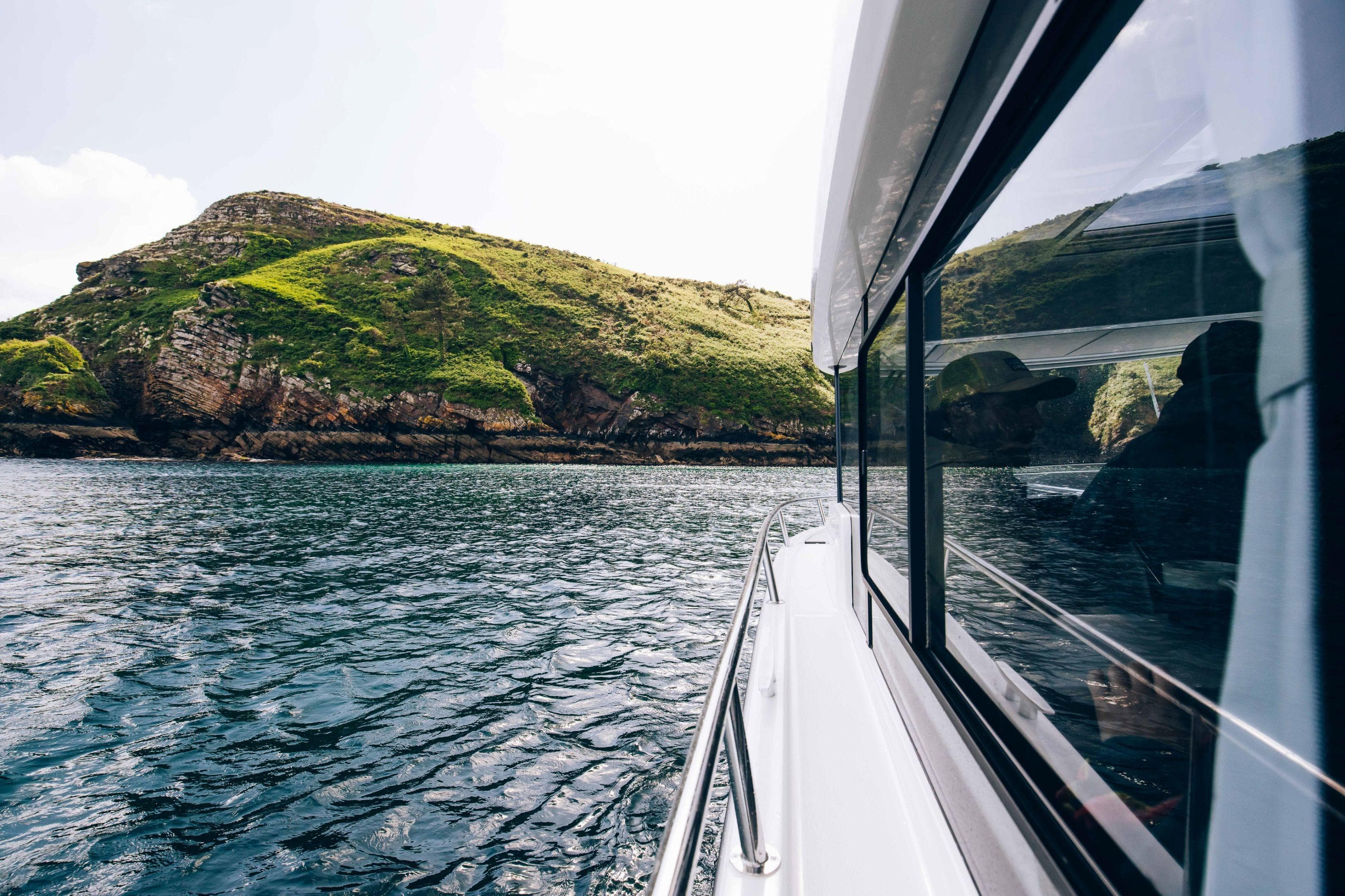 2026 Jeanneau NC 895 Sport Series 2 cruising near a lush, rocky island.