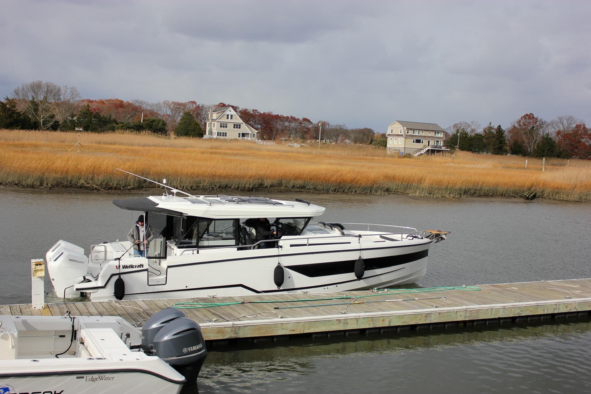 2026 Wellcraft 38 Explorer docked by a scenic riverside with autumn foliage.