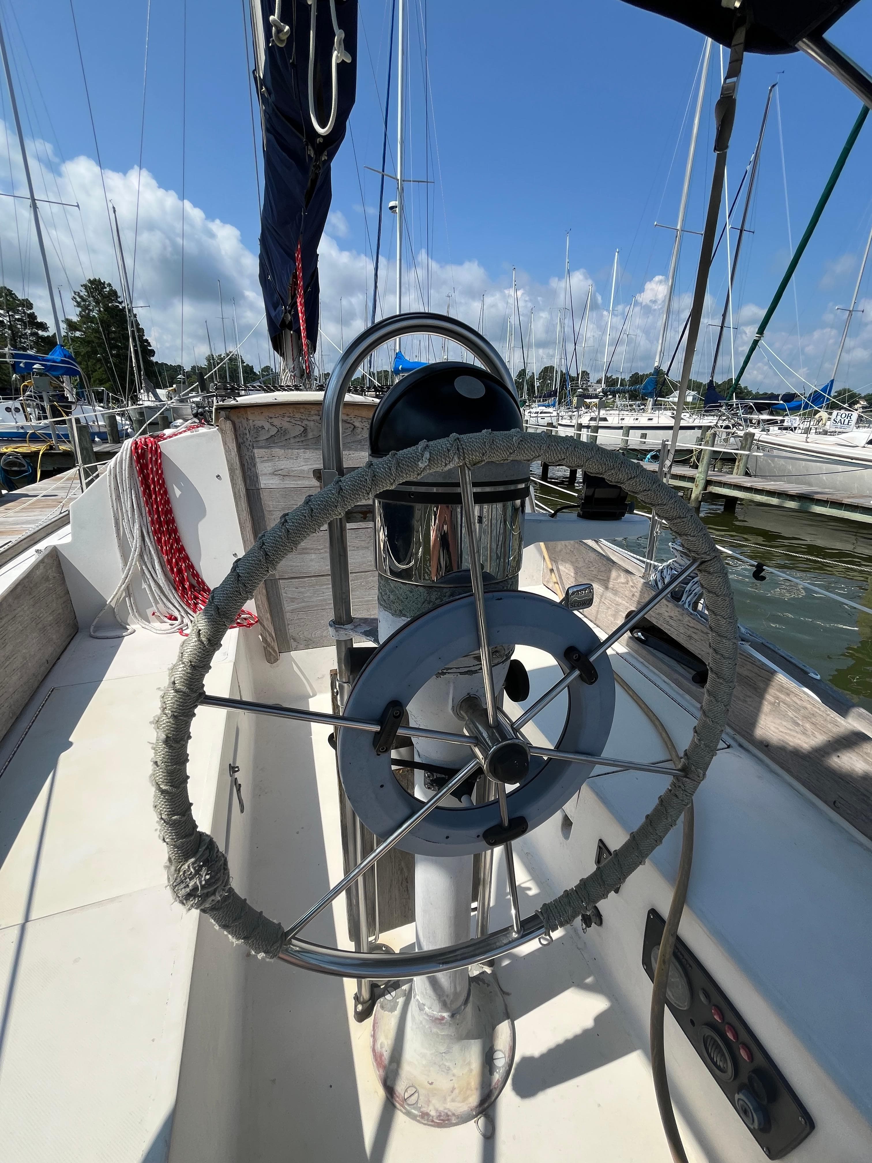 1978 Bristol 29.9 sailboat helm with marina background, featuring a wrapped steering wheel.
