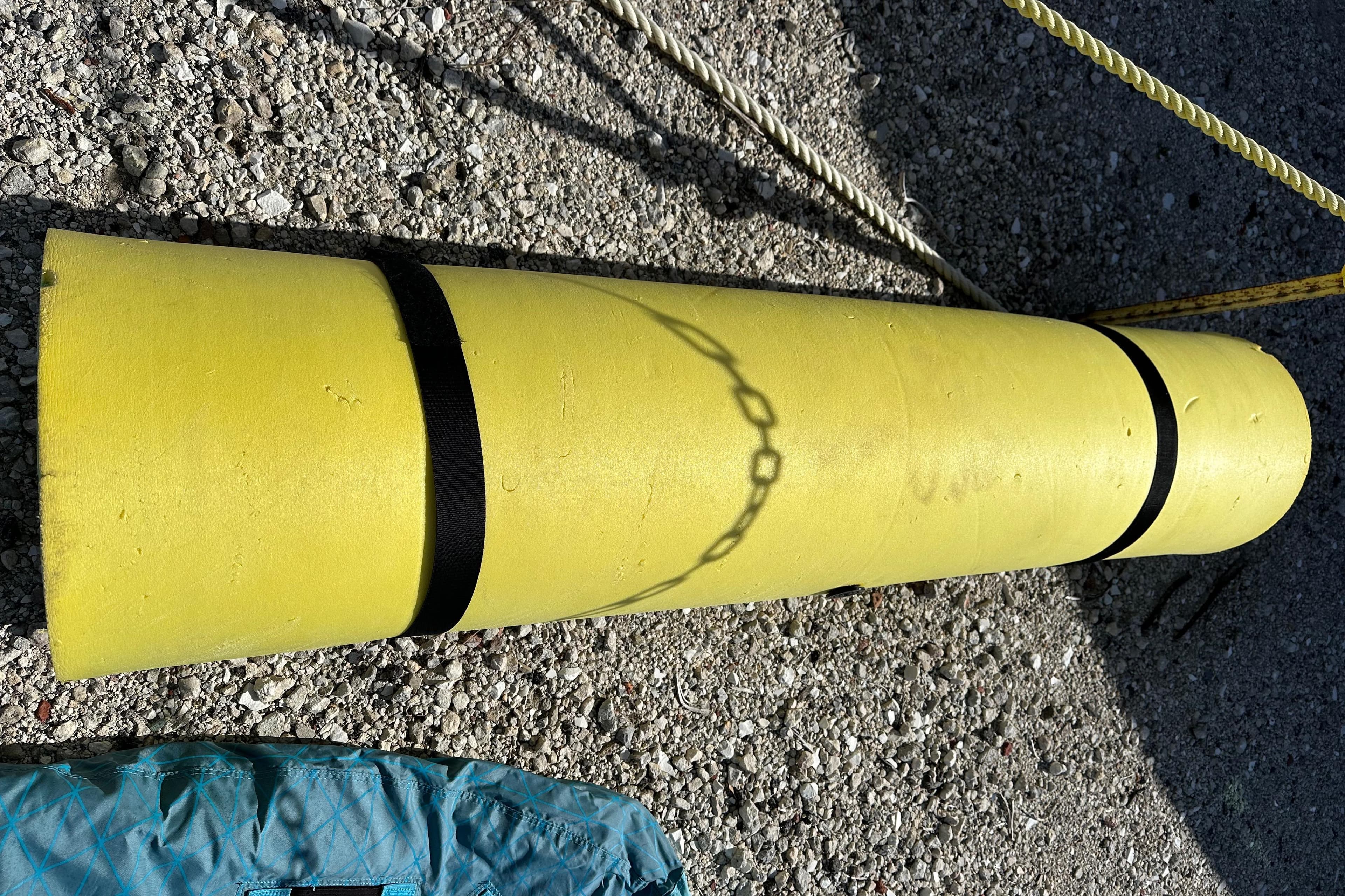 Yellow cylindrical object with black straps on gravel, near ropes and a blue item.
