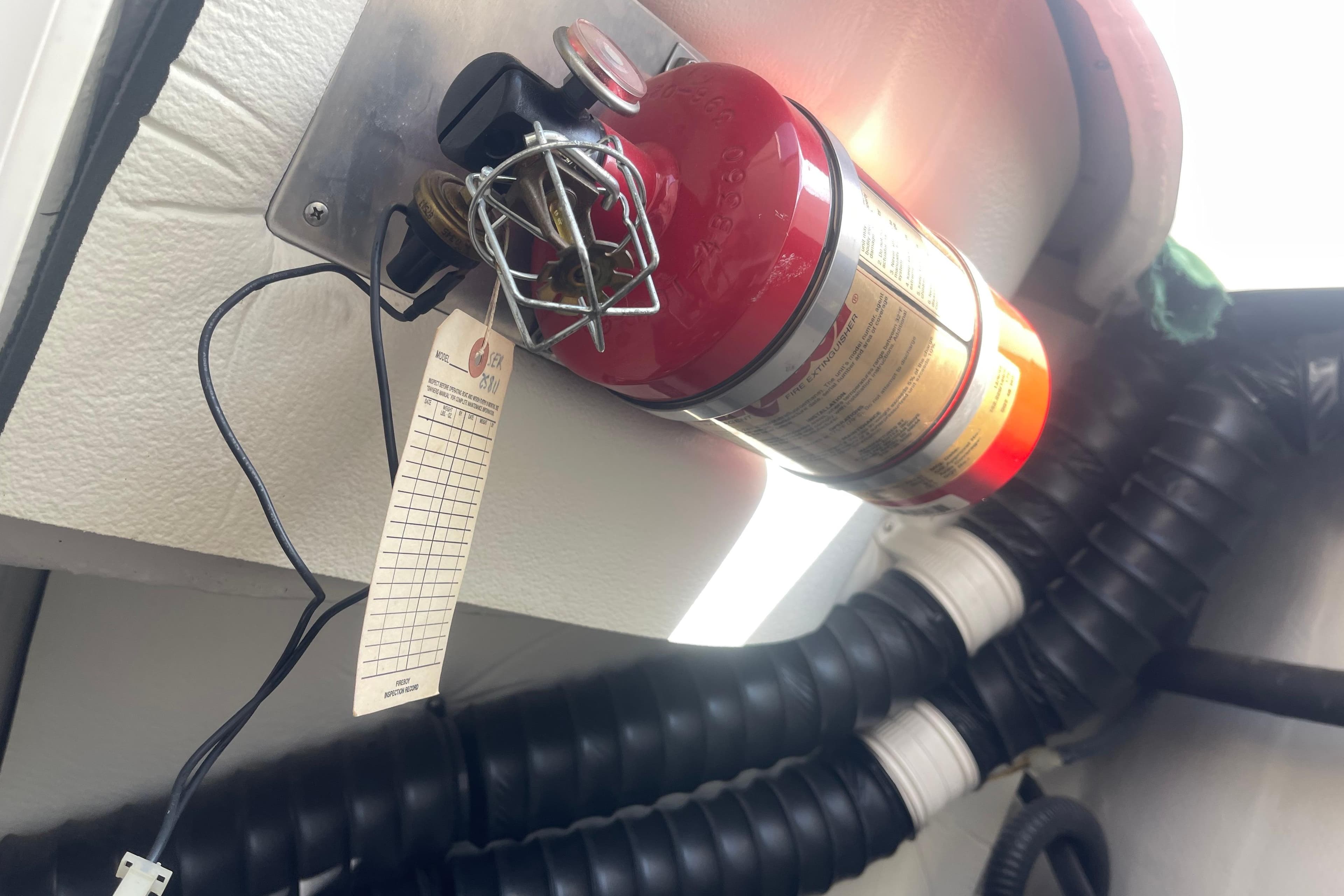 Fire extinguisher mounted on a 2004 Cobalt 282 boat, with inspection tag attached.