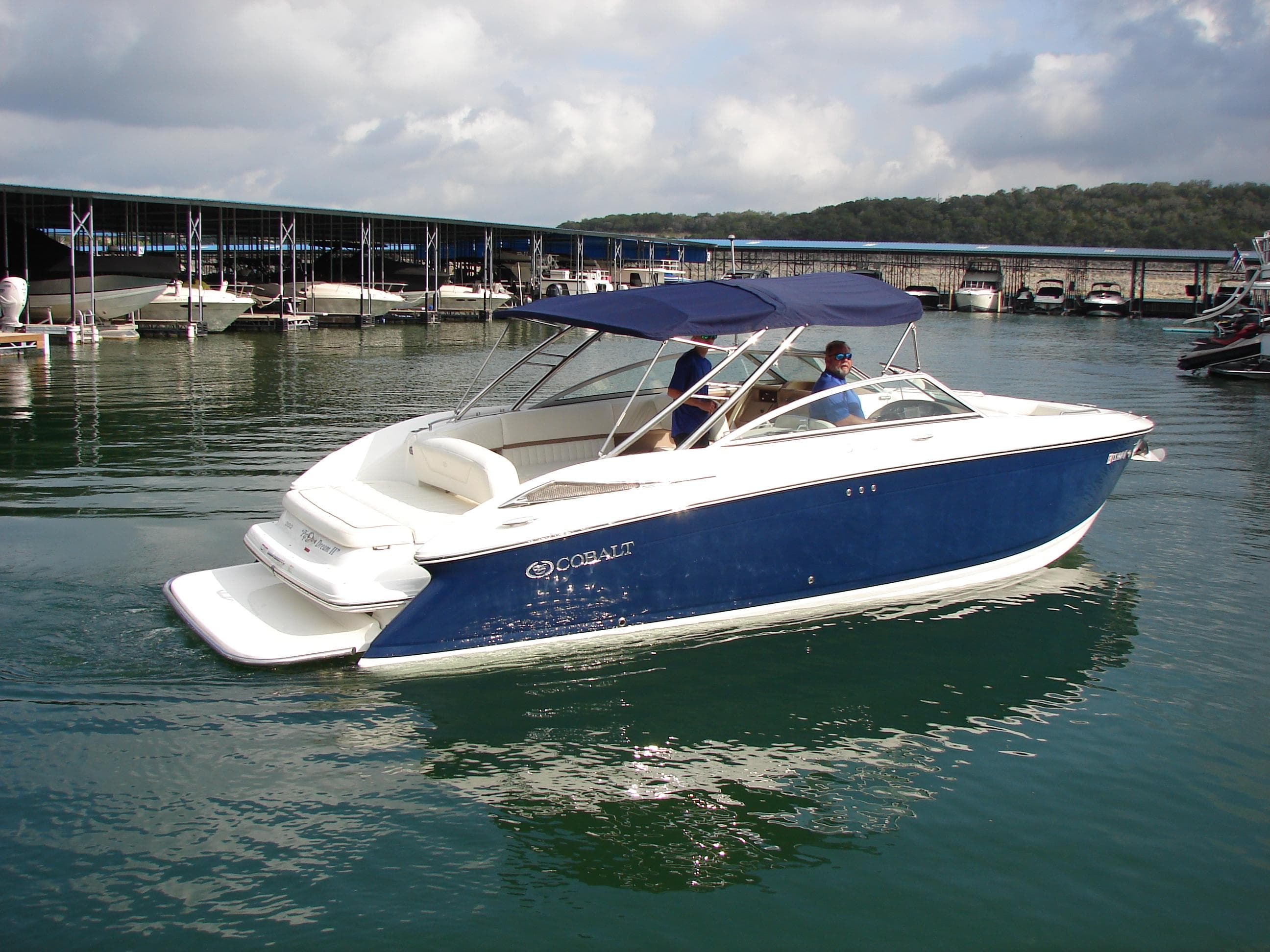 2007 Cobalt 302 boat on calm water near a marina, featuring a blue and white design.