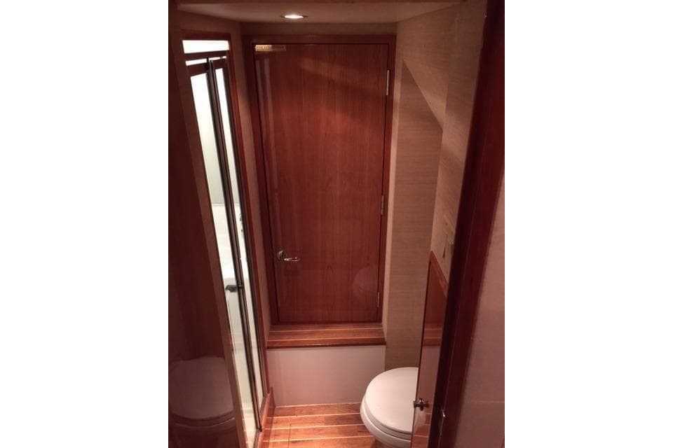 Bathroom interior of 2004 Hatteras 65 Convertible yacht with wooden door and flooring.