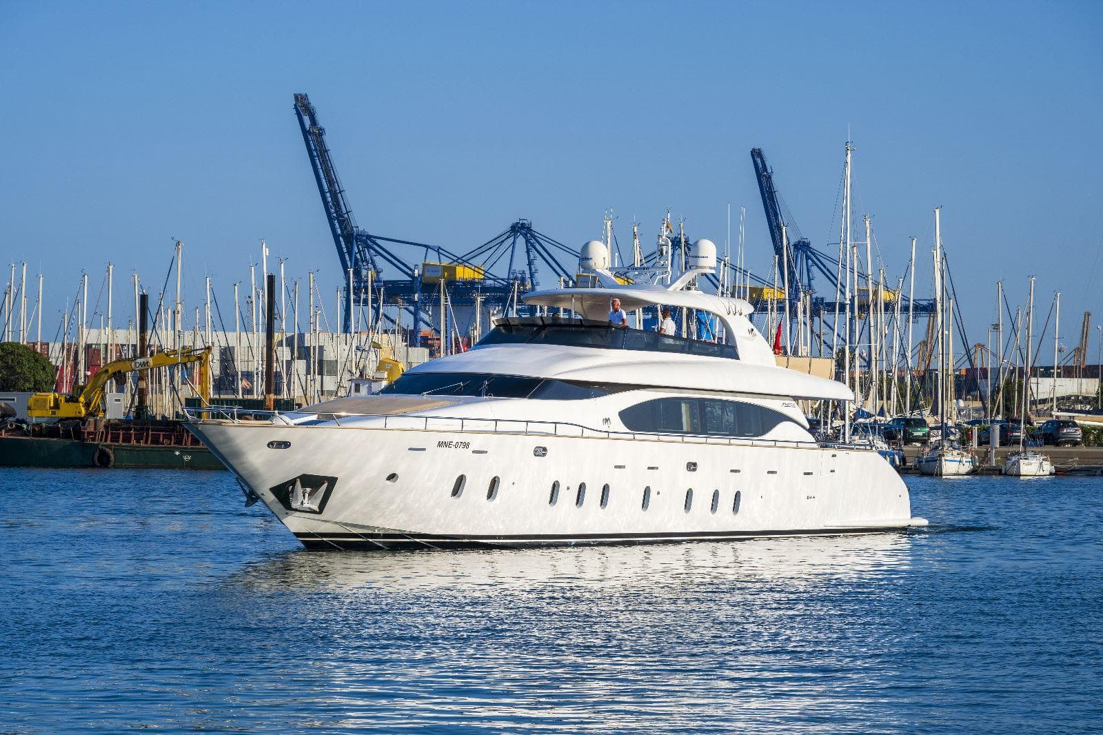Luxurious 2011 Maiora 27 yacht cruising in a bustling marina with cranes and sailboats.