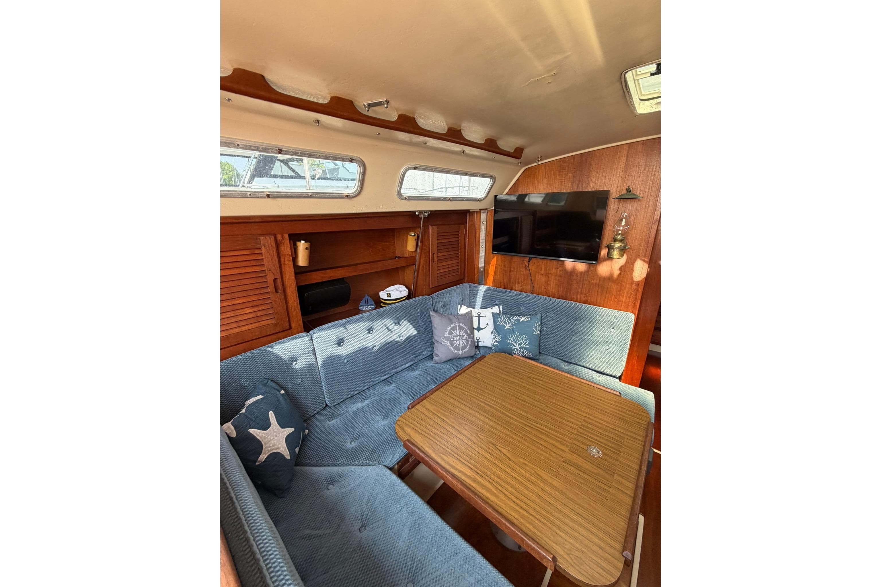 Cozy interior of 1985 Catalina 36 sailboat with blue seating and wooden table.