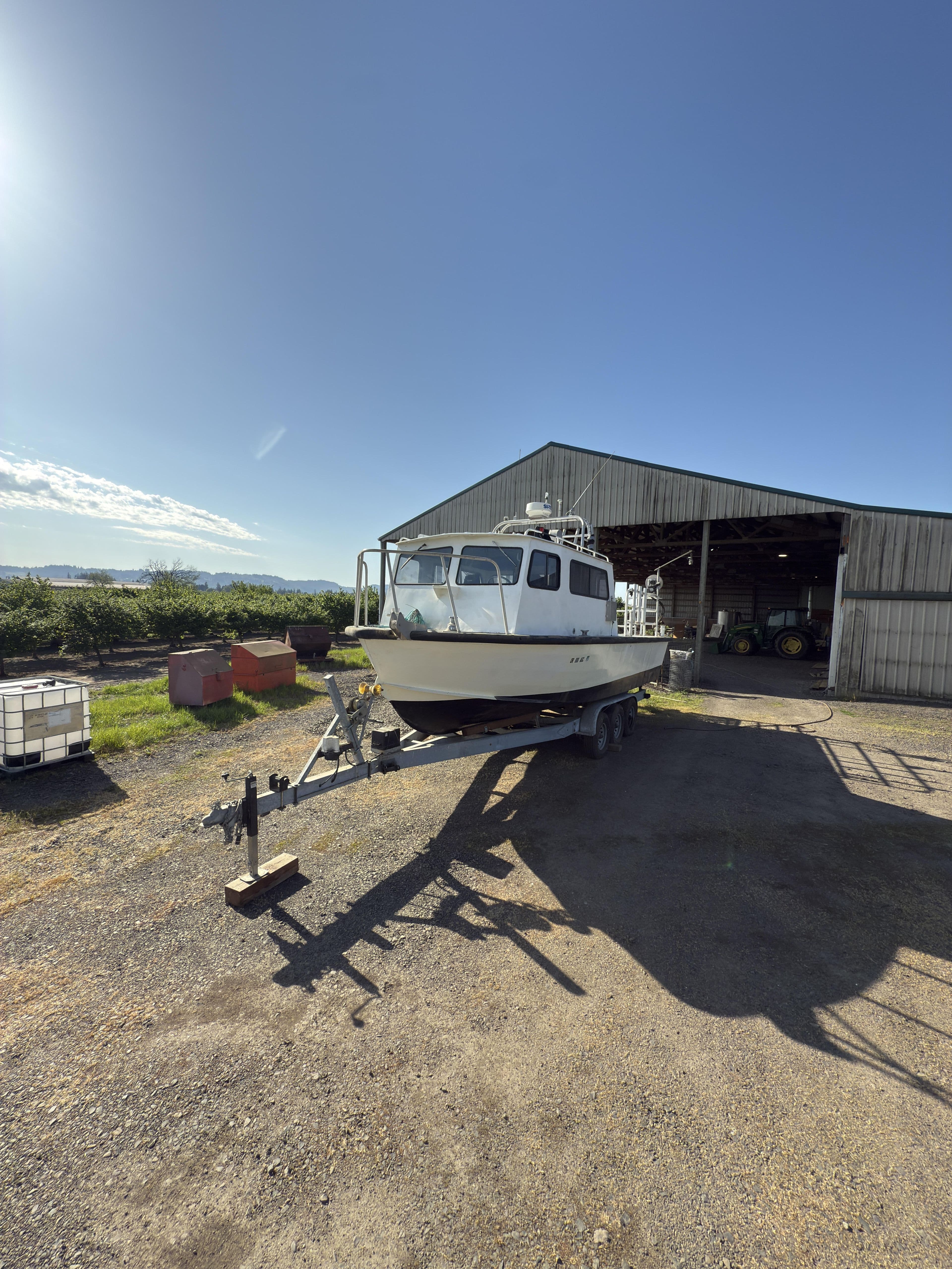 1975 Monark 30 Fishing Boat on trailer near barn under clear blue sky.