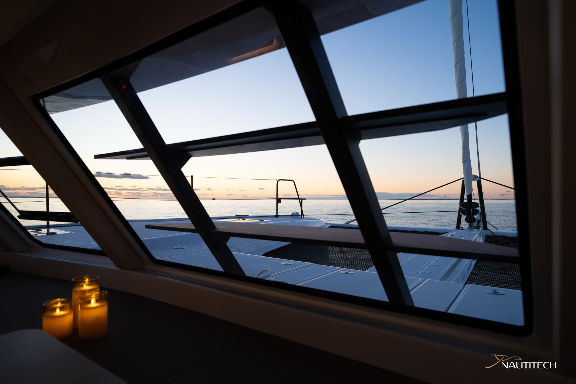2025 Nautitech 48 Open yacht interior with ocean view at sunset, featuring lit candles.