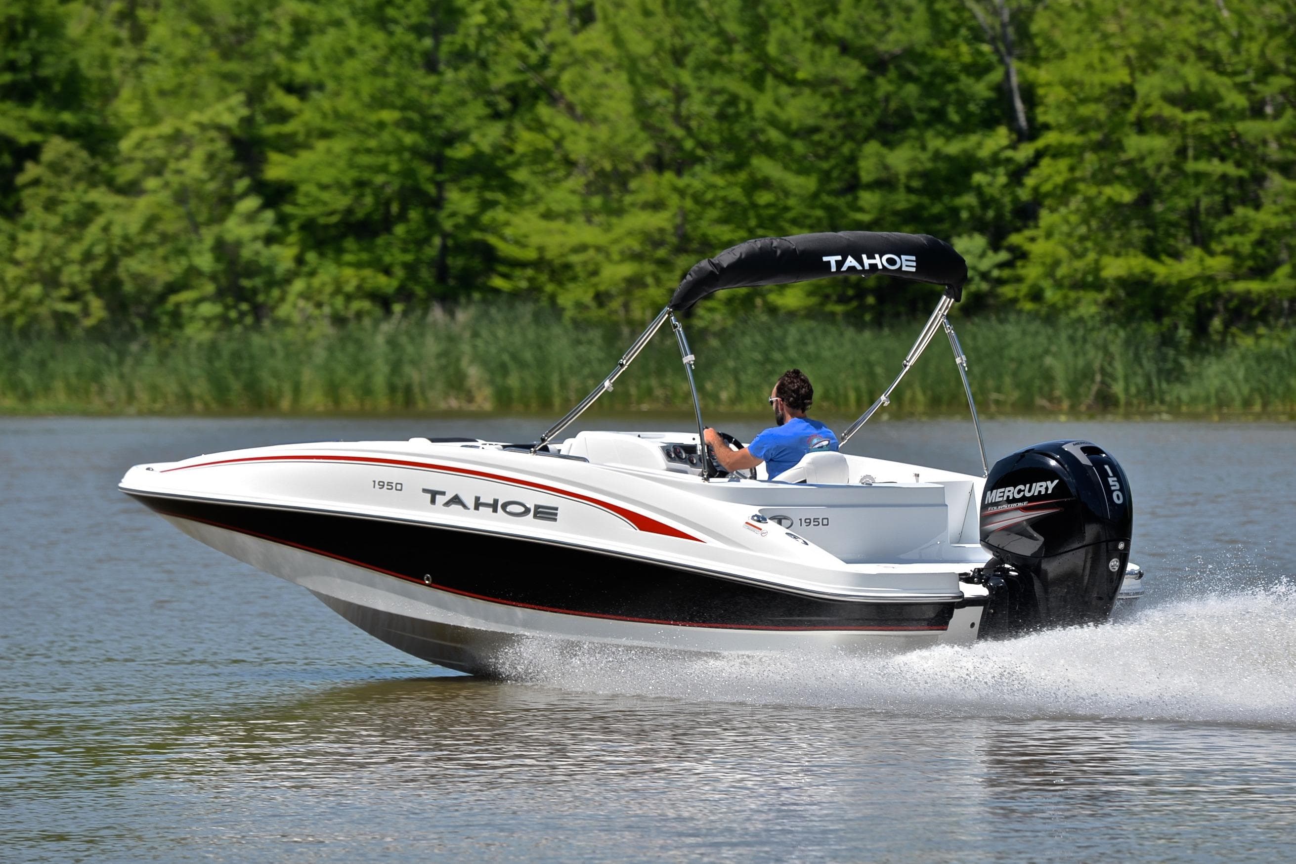2018 Tahoe 1950 boat cruising on a lake with lush green trees in the background.