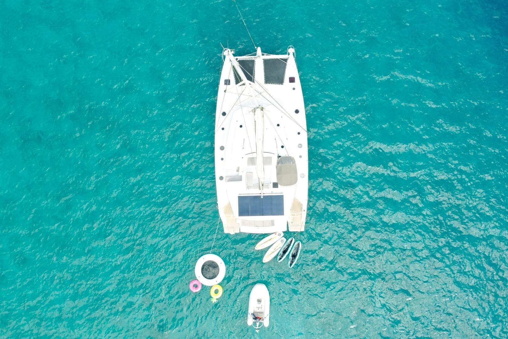 Aerial view of 2013 Fountaine Pajot Sanya 57 catamaran on turquoise water with inflatables.