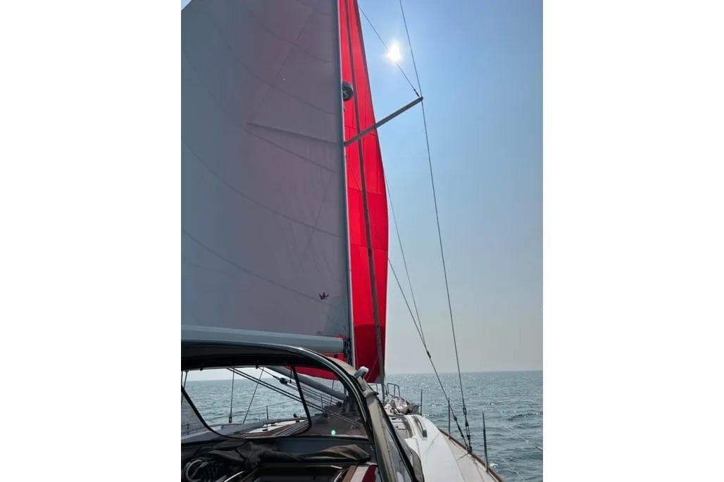 Sailing on a 2016 Bavaria Vision 46 yacht with vibrant red sails under a clear sky.