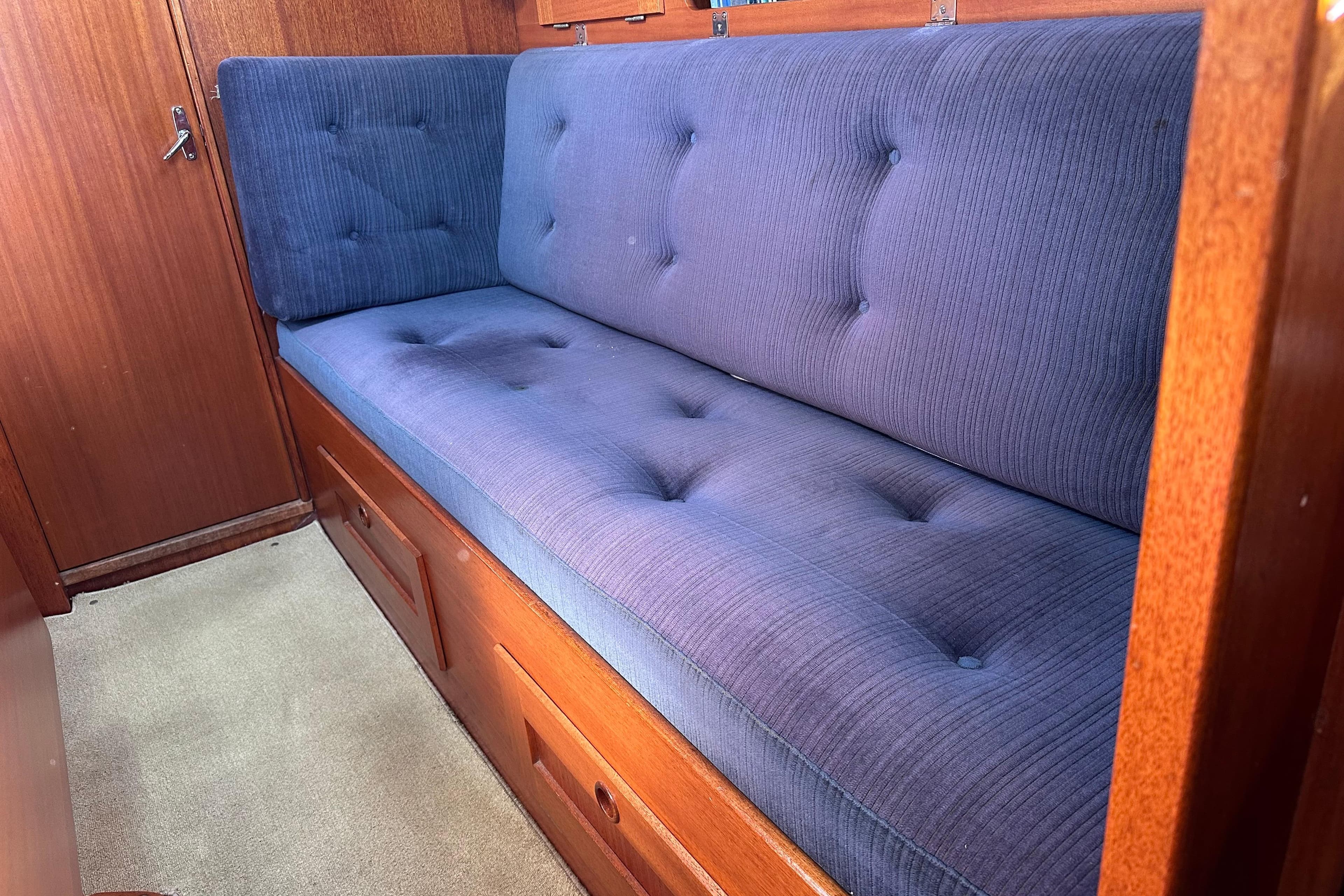 Interior of 1987 Hallberg-Rassy 94 Kutter with blue cushioned seating and wooden paneling.