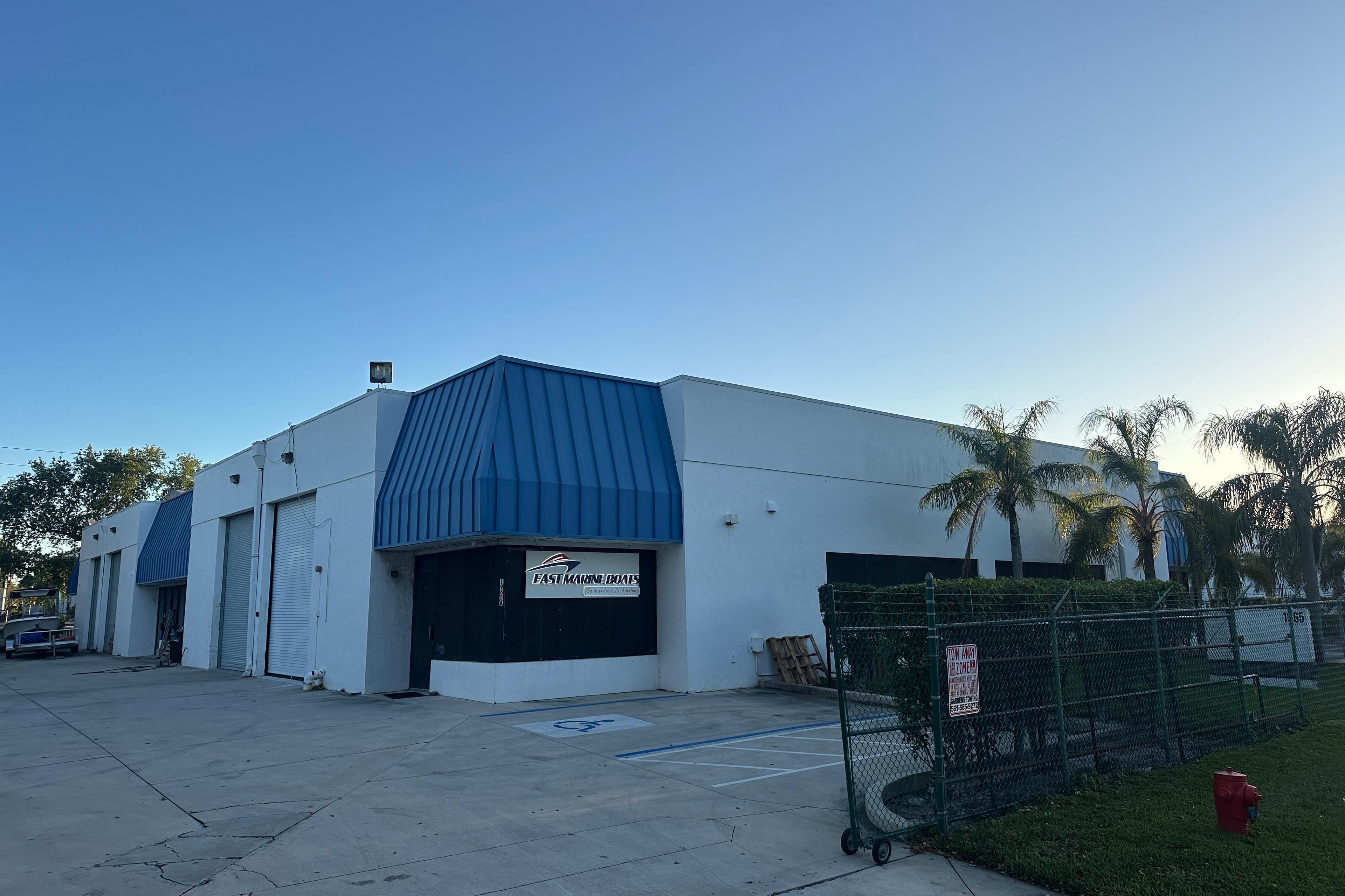 Exterior view of East Marine Boats facility with palm trees and blue awnings.