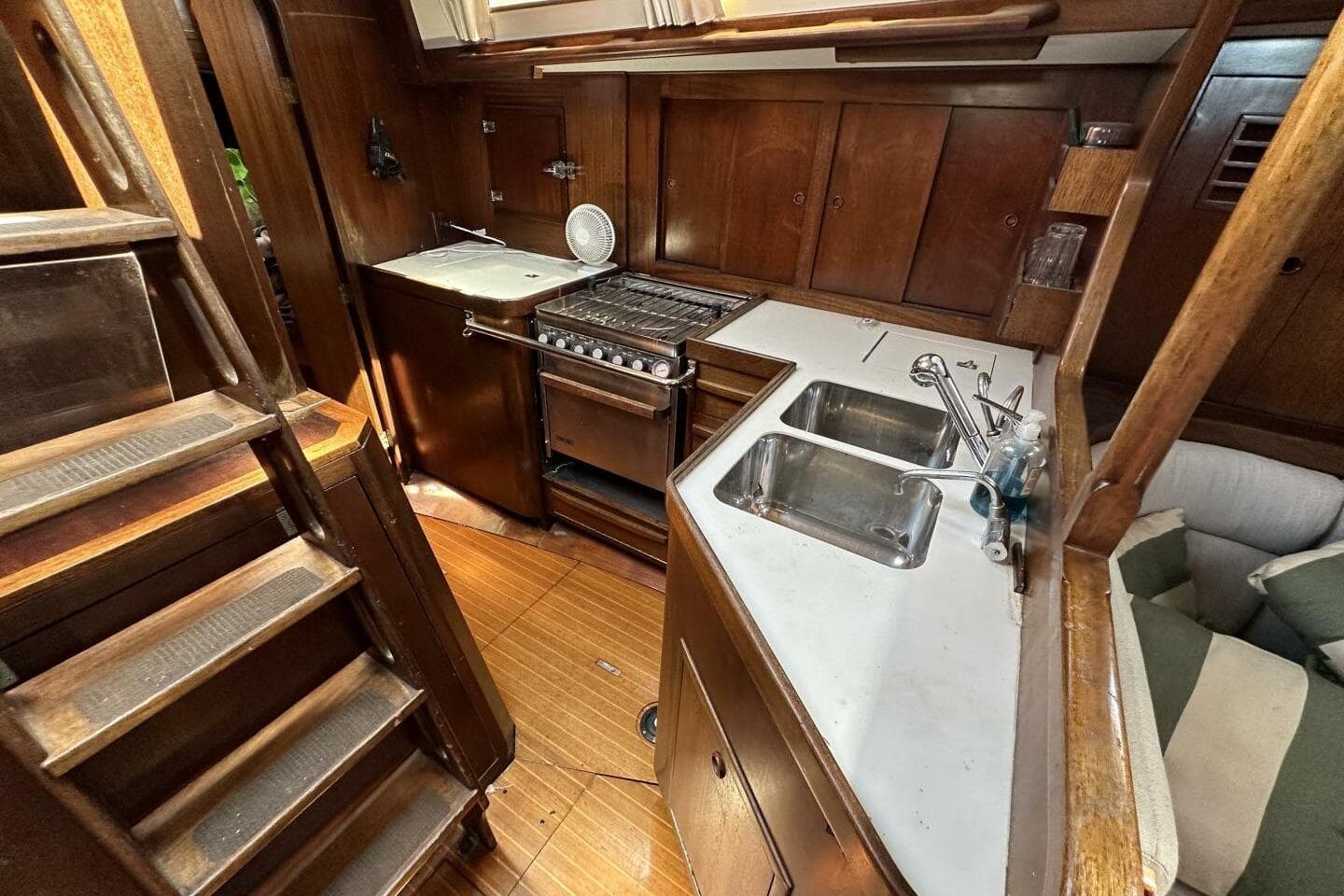 1988 Cambria 46 yacht interior kitchen with wooden cabinetry, stove, and dual sink.