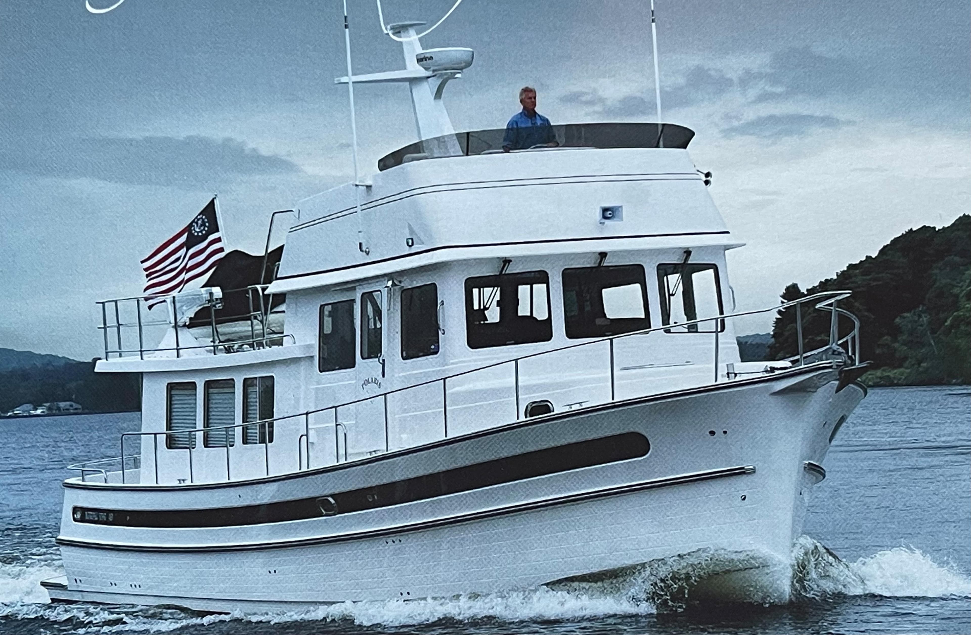 2025 Nordic Tug 49 cruising on water with American flag, overcast sky.