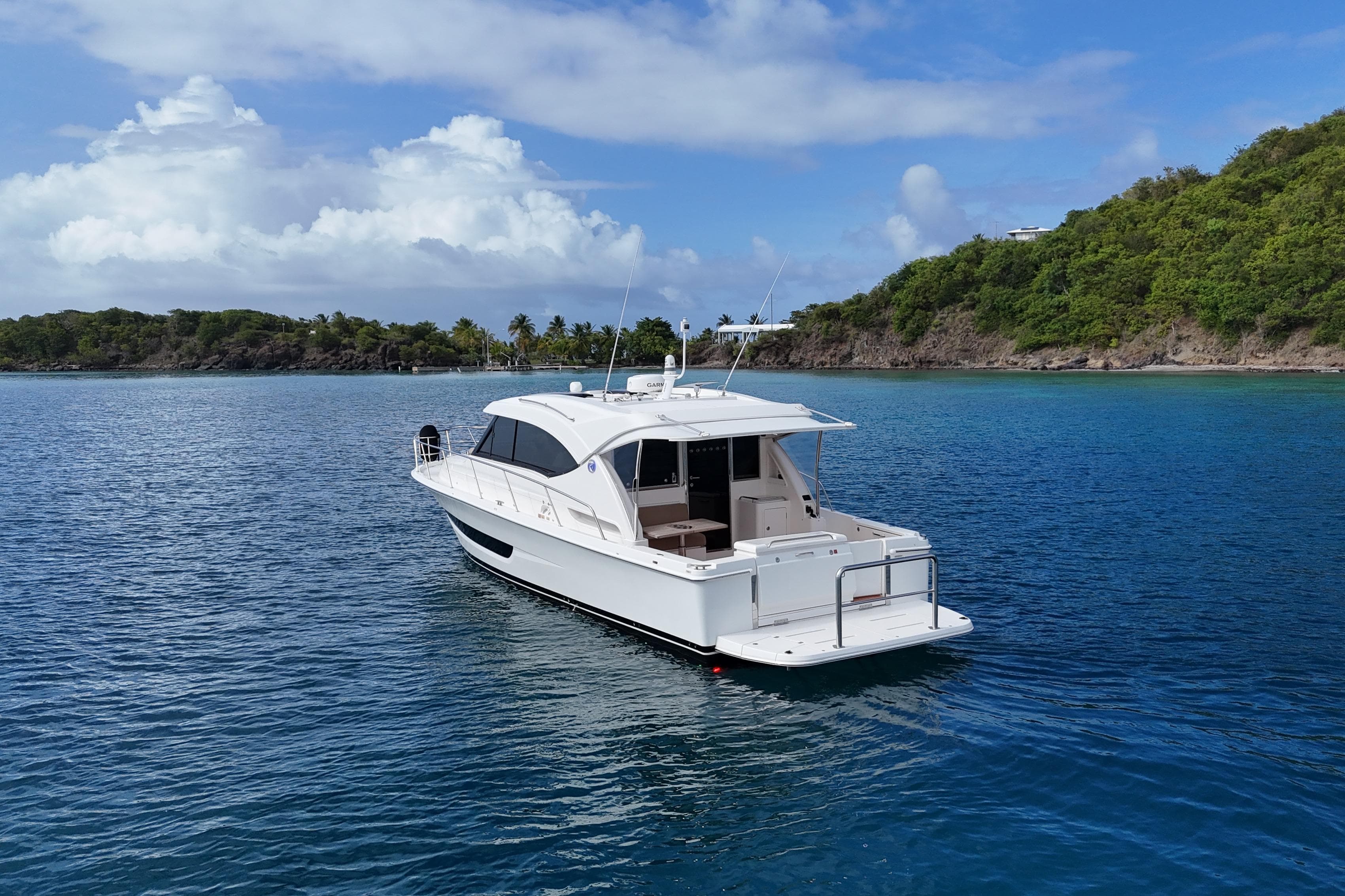2020 Riviera 395 SUV yacht on serene blue waters near lush green coastline.
